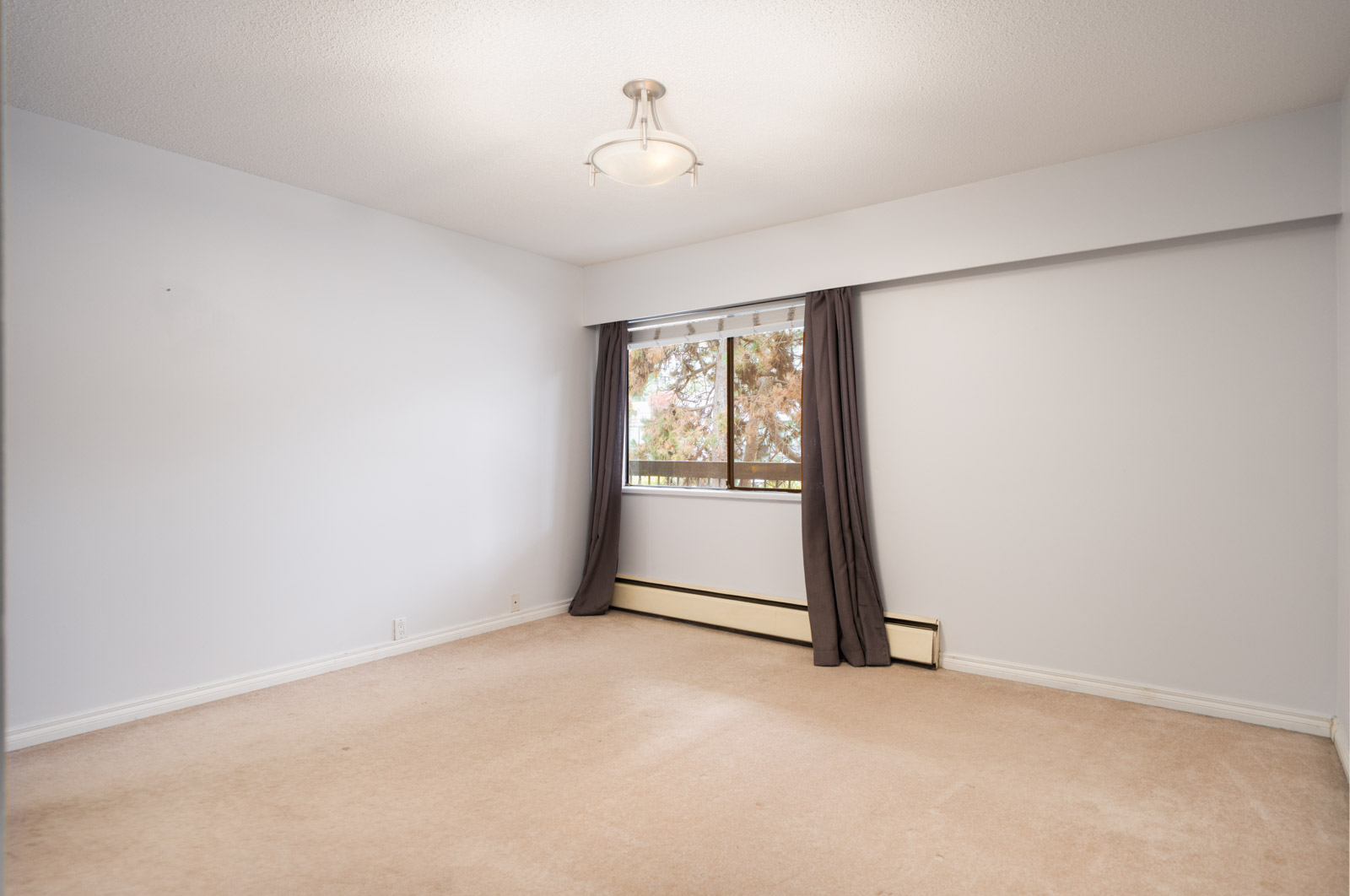 Empty 2nd floor room with beige carpet, white walls, ceiling light, large window with dark curtains, and baseboard heater in Richmond near Buswell.