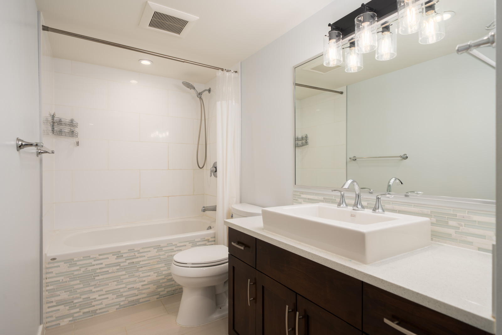 Modern Richmond bathroom featuring a bathtub-shower combo, white tile, dark wood vanity, vessel sink, large mirror, and four-light fixture.
