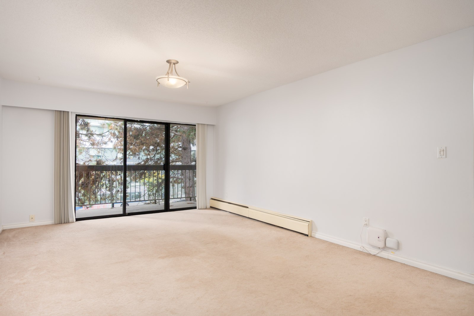 Unfurnished living room with beige carpet, white walls, ceiling light, and sliding glass door to balcony with trees in Richmond on Buswell.