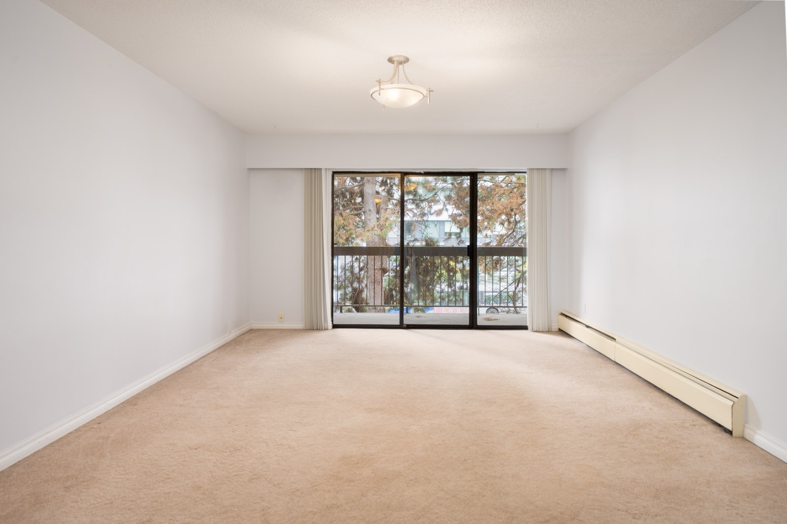 Empty second-floor room in Richmond’s Buswell area with beige carpet, white walls, ceiling light, and large window overlooking trees.