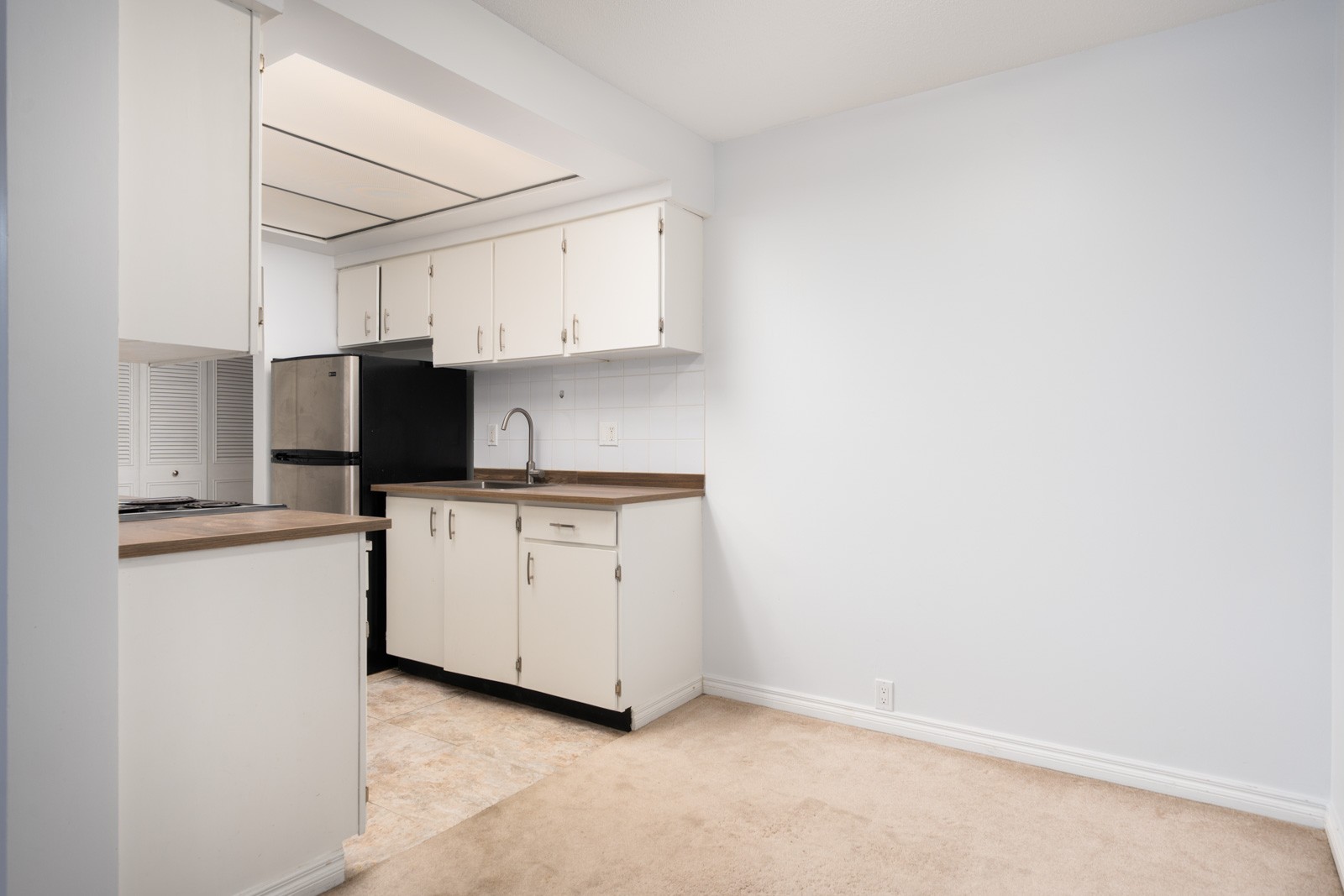 Small kitchen with white cabinets, wood counters, stainless sink, black fridge, and beige carpeted dining area in Richmond Buswell.