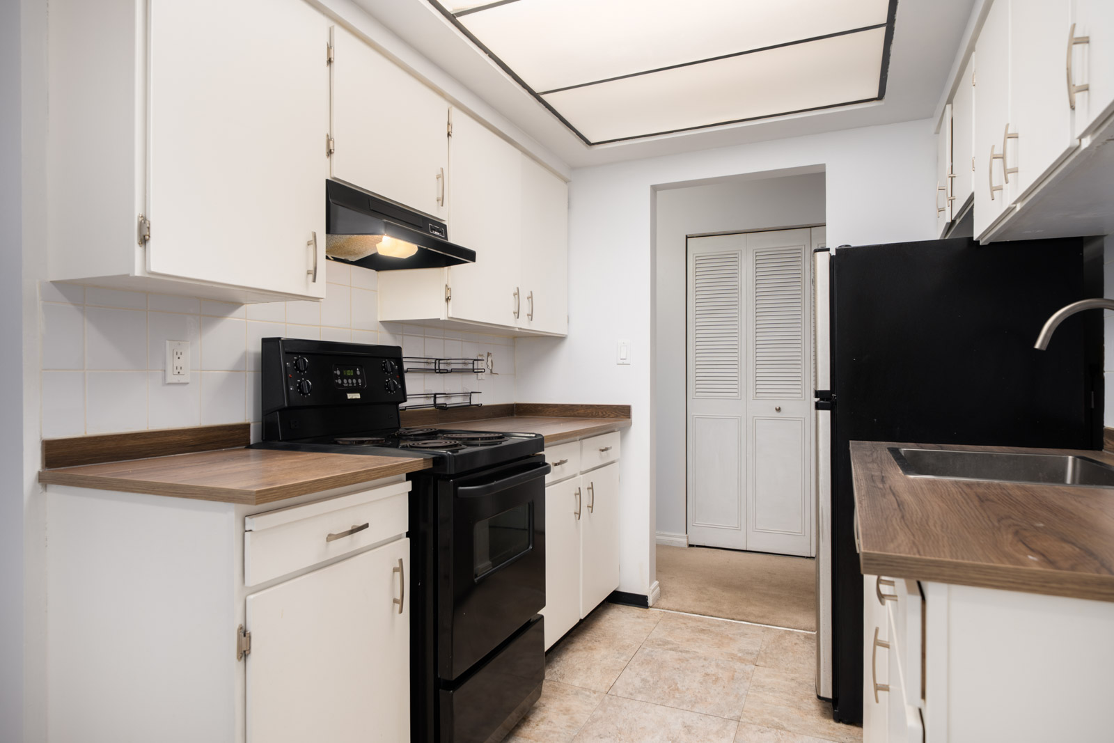 Galley kitchen in a Richmond home near Buswell, featuring white cabinets, black appliances, wood counters, and tile flooring.