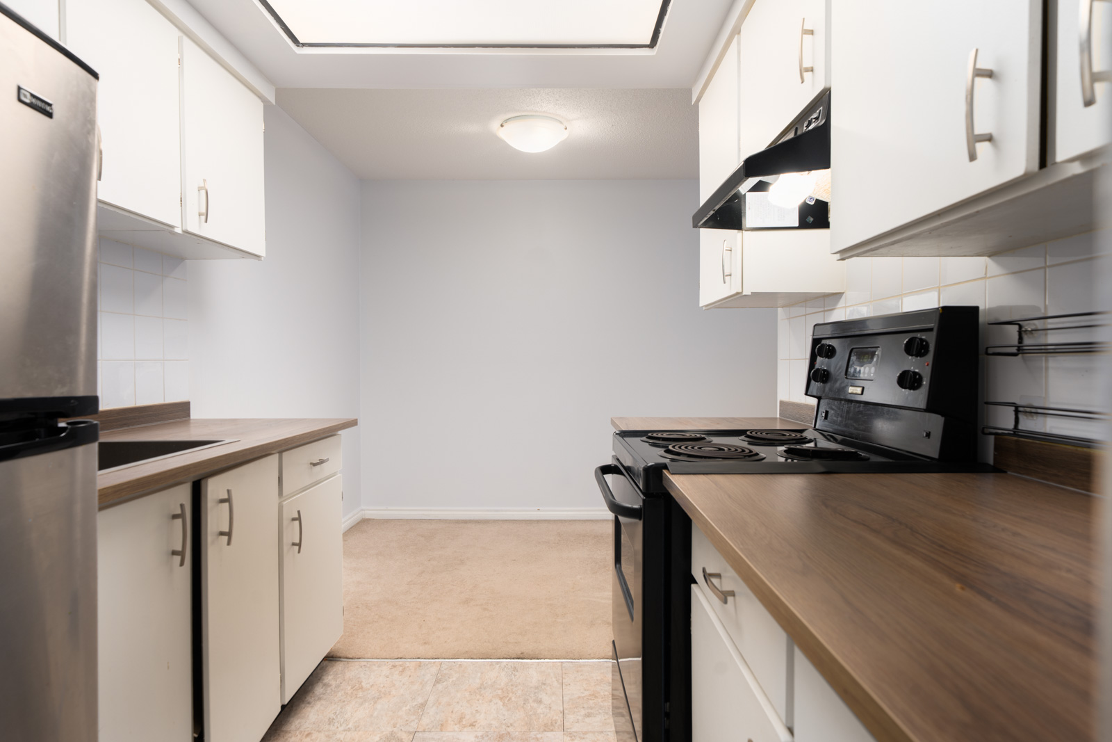 Galley kitchen at 6560 Buswell in Richmond with white cabinets, brown counters, black stove, stainless fridge, and dining area.