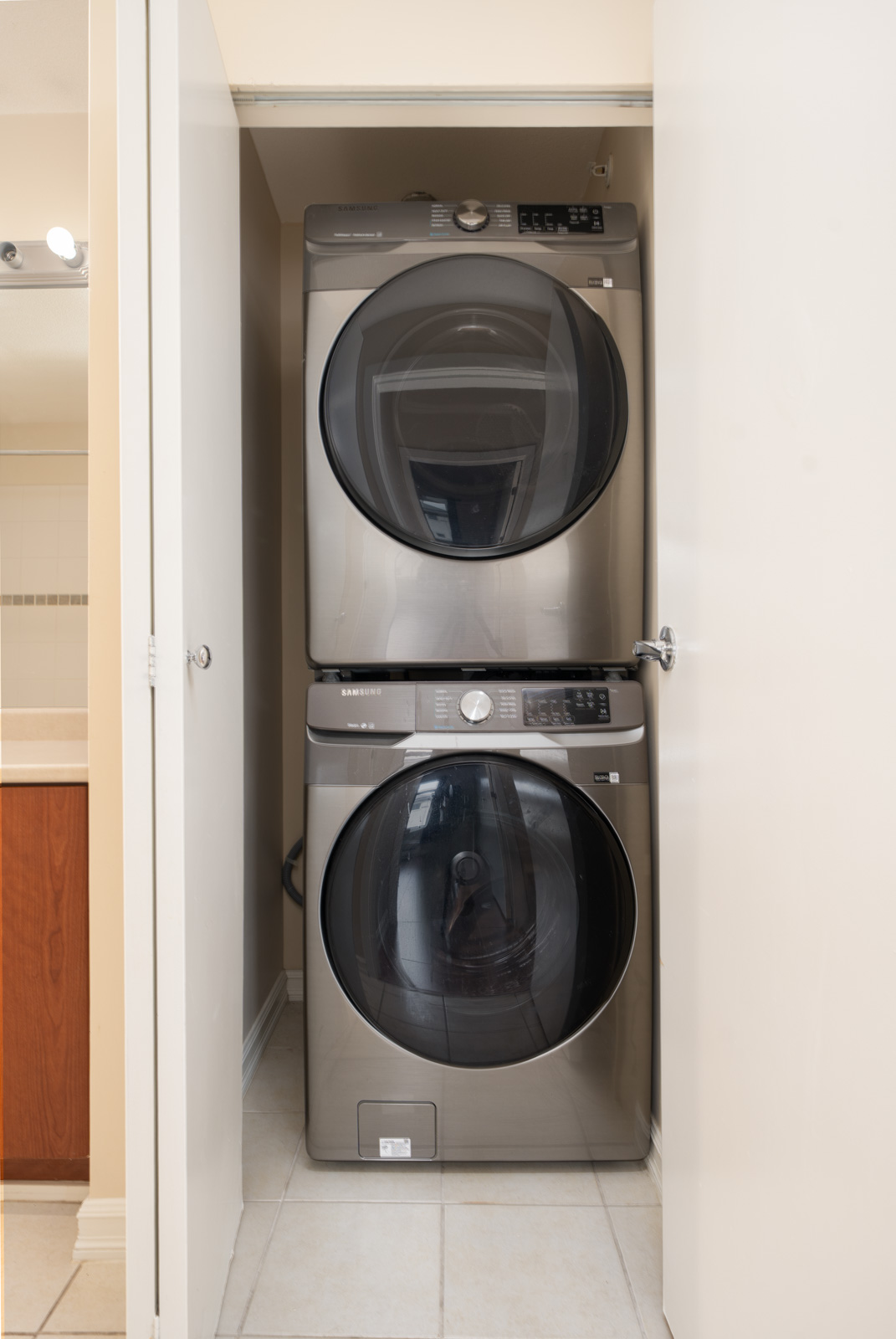 Stacked front-load washer and dryer in a narrow tiled laundry closet with open doors in a Surrey home at 10088 148 Street.
