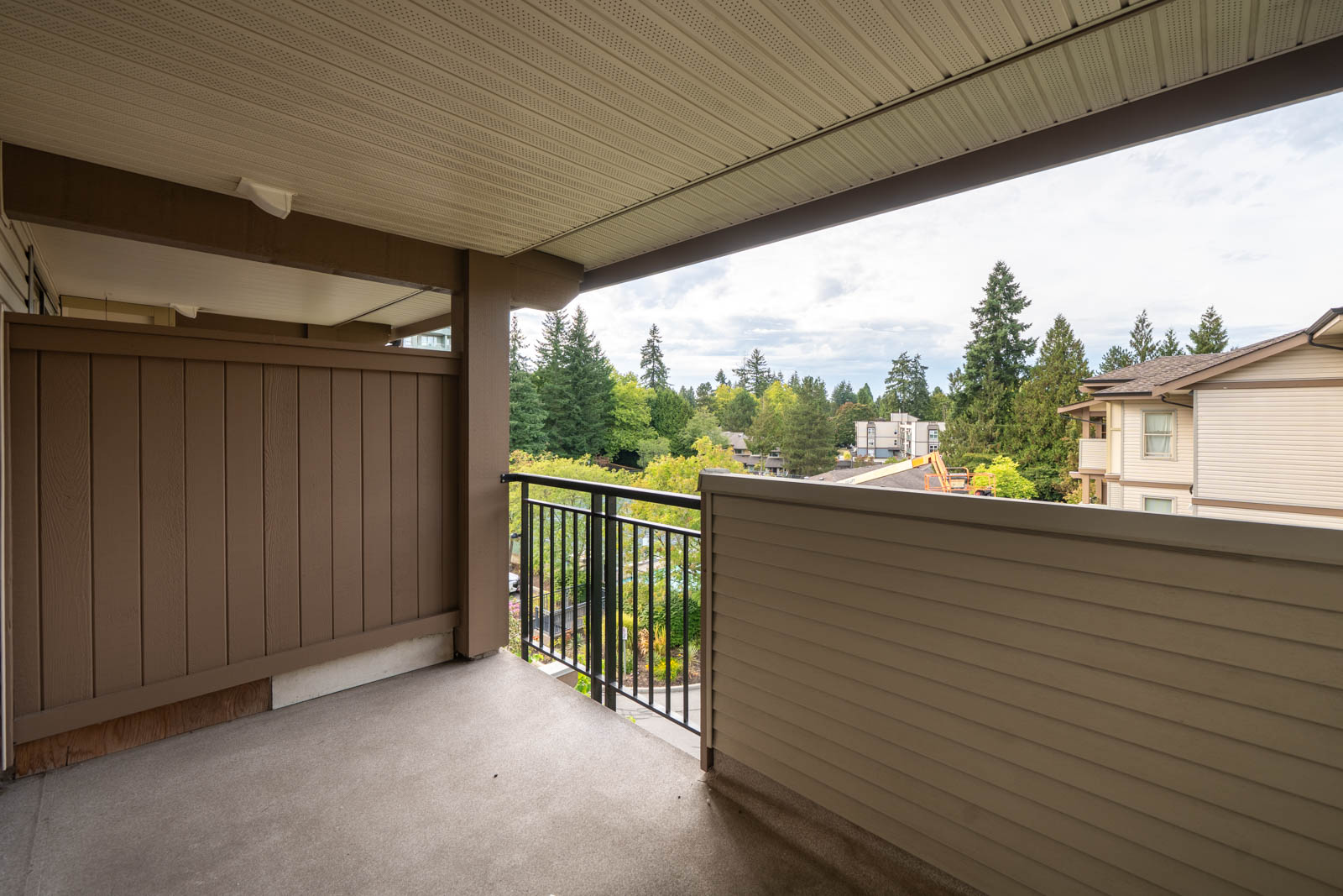 Covered apartment balcony with beige siding, black railing, and skyline view on 4th floor at 10088 148 St, Surrey.