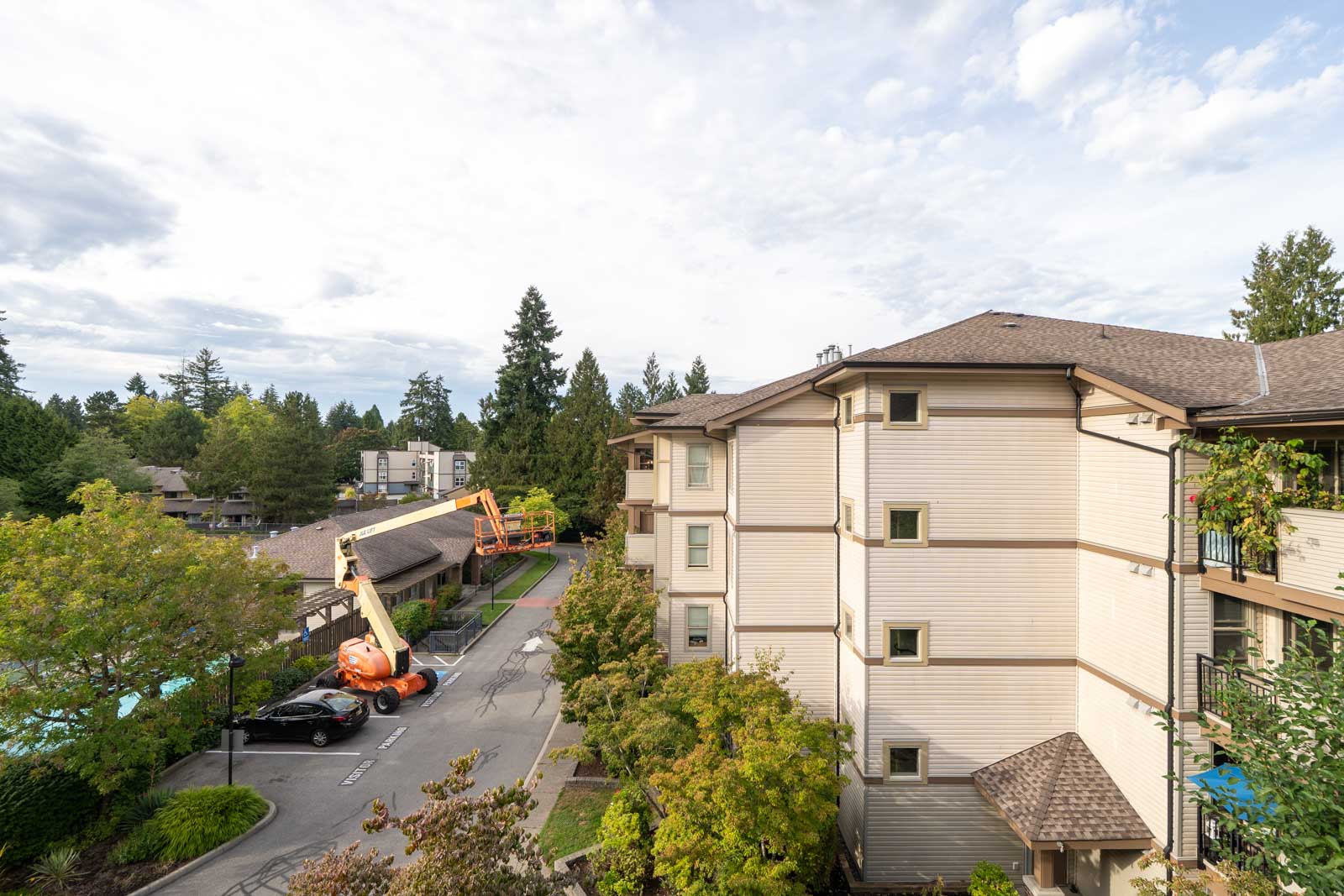 Beige apartment building in Surrey near 148 St at 10088, surrounded by trees, with construction gear and a car below.