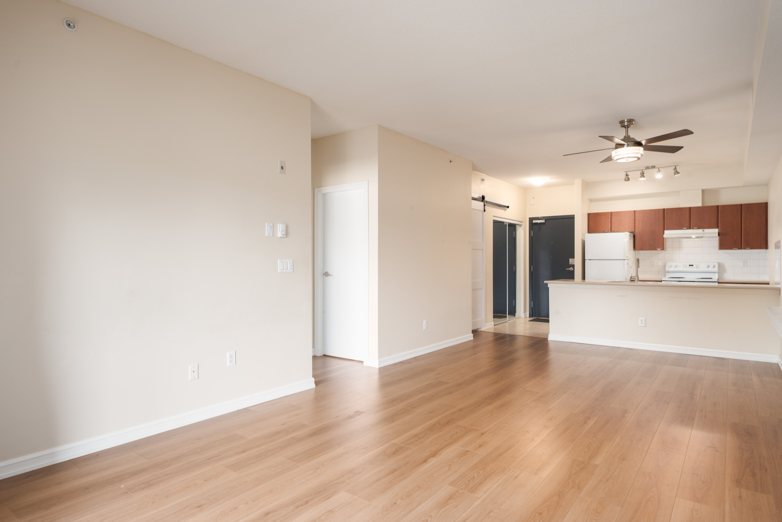 Empty Surrey apartment on 148 Street with light wood floors, beige walls, open kitchen, white appliances, blue and white doors.