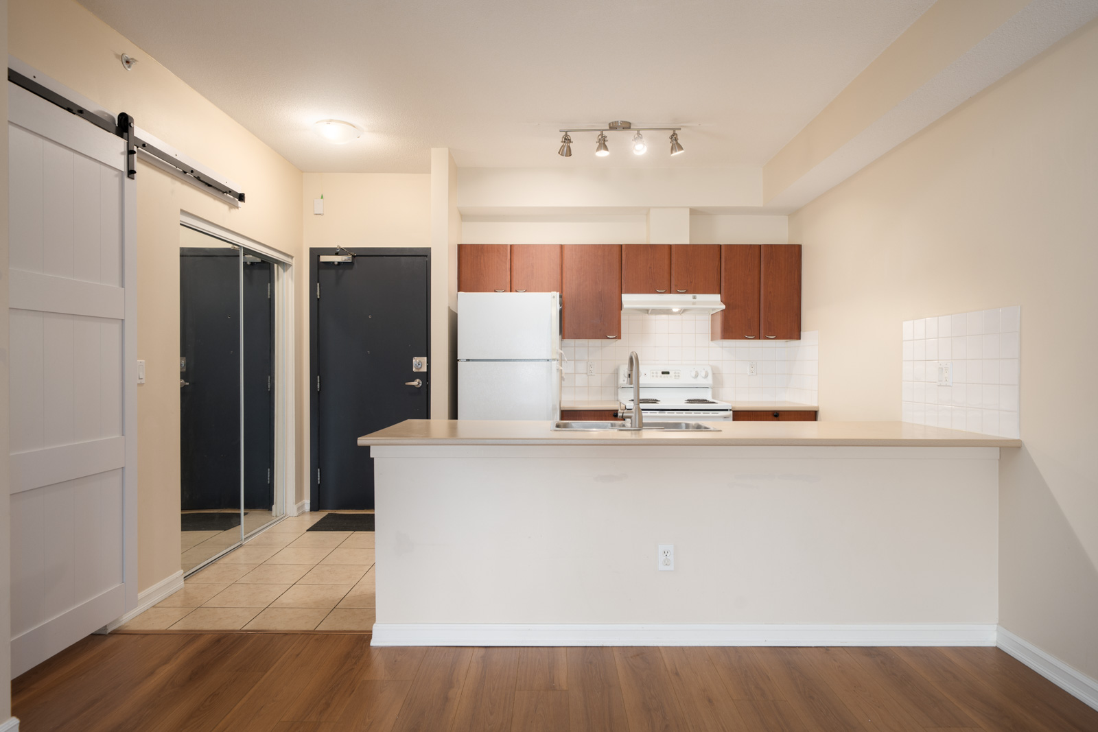 Modern Surrey kitchen with brown cabinets, white appliances, light countertops, sliding barn door, and wood-tile flooring. 10088 148 St.