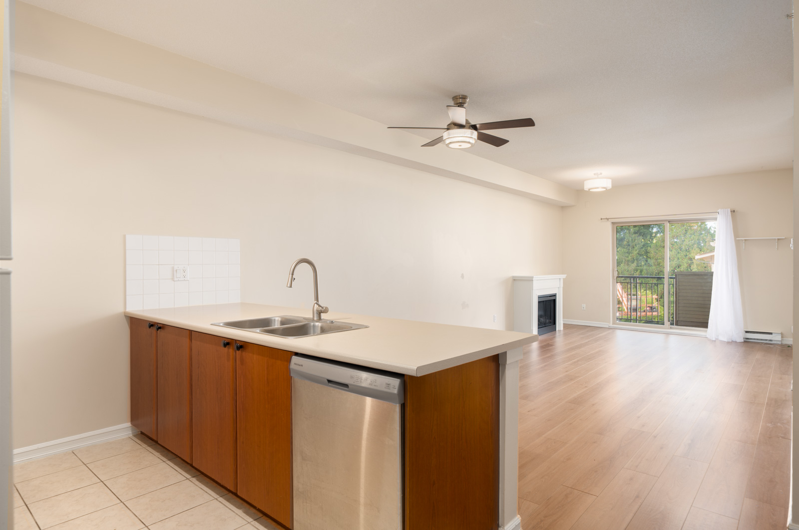 Unfurnished open-plan kitchen and living area with wood floors, ceiling fan, fireplace, and balcony overlooking trees in Surrey near 148 St.