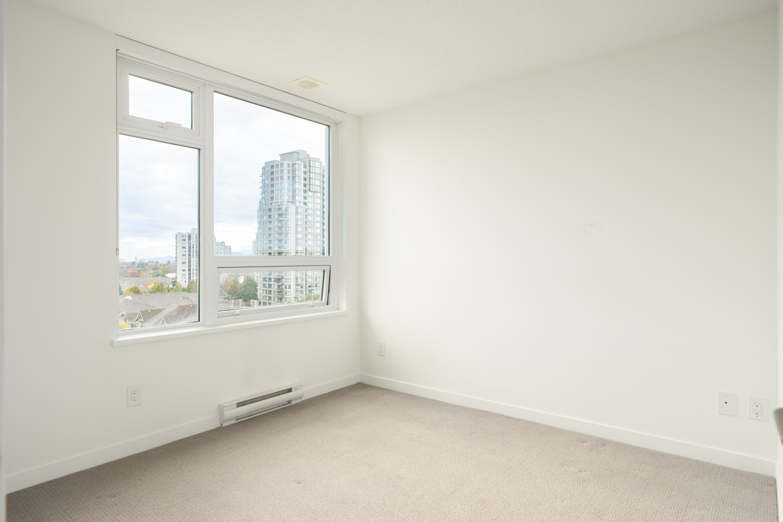 Empty room with white walls, beige carpet, and a large window on the 8th floor at 5515 Boundary Rd, Vancouver, overlooking city buildings.