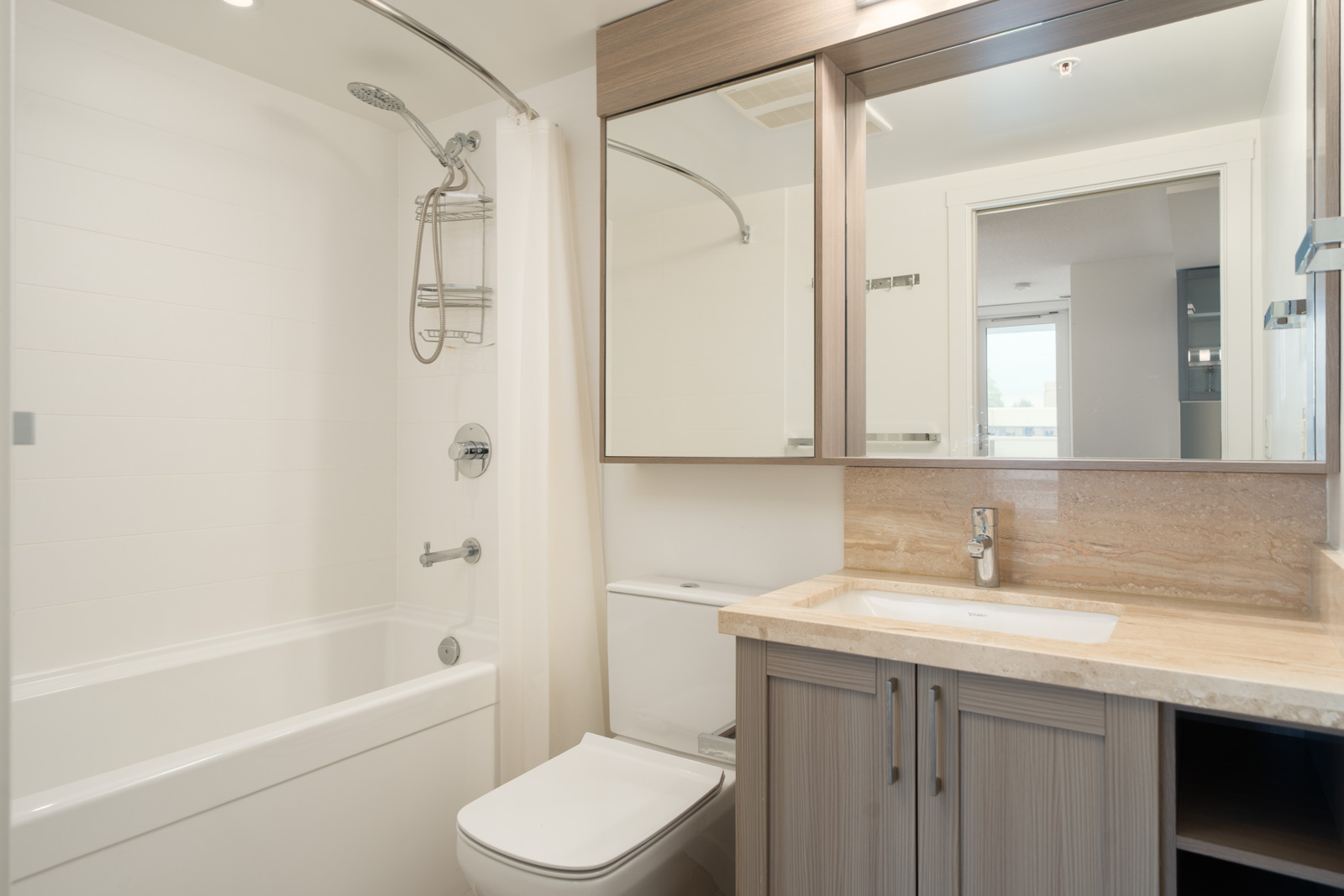 Modern bathroom on Boundary Rd, Vancouver, with a tub-shower combo, toilet, marble sink, large mirror, and neutral cabinets.