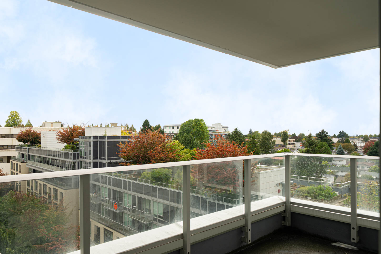 View from a high balcony on Boundary Rd, Vancouver: modern apartments, glass railings, and autumn trees beneath a partly cloudy sky.