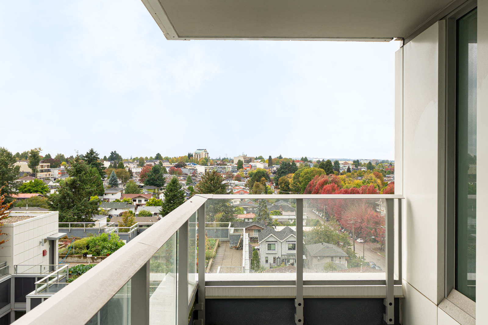 Balcony with glass railing overlooking trees and houses in a Vancouver neighborhood near Boundary Rd, under partly cloudy sky.