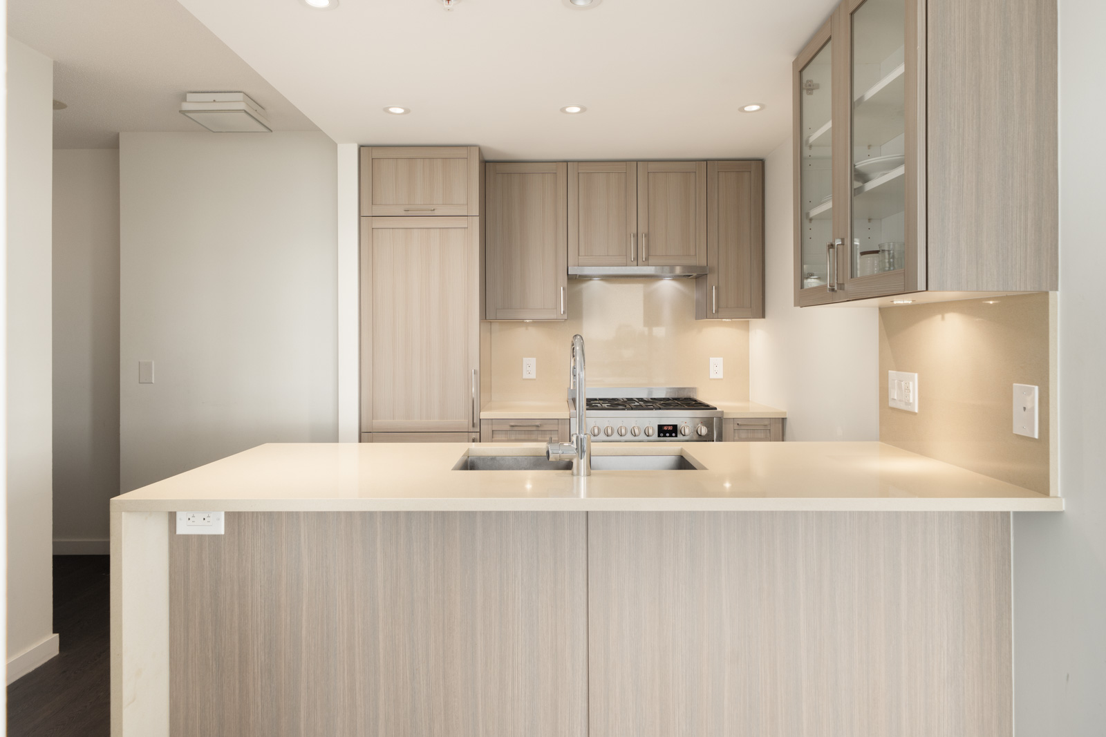 Light wood kitchen with built-in stove, stainless sink, under-cabinet lights, seen from island on 8th floor at 5515 Boundary Rd, Vancouver.