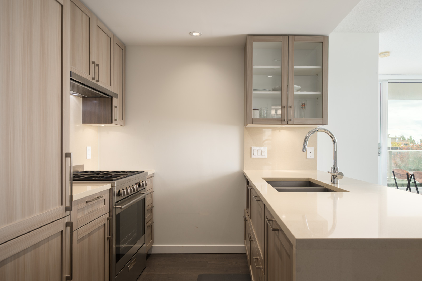 Modern kitchen with light wood cabinets, stainless appliances, beige counters, island sink, and sliding glass door in Vancouver.