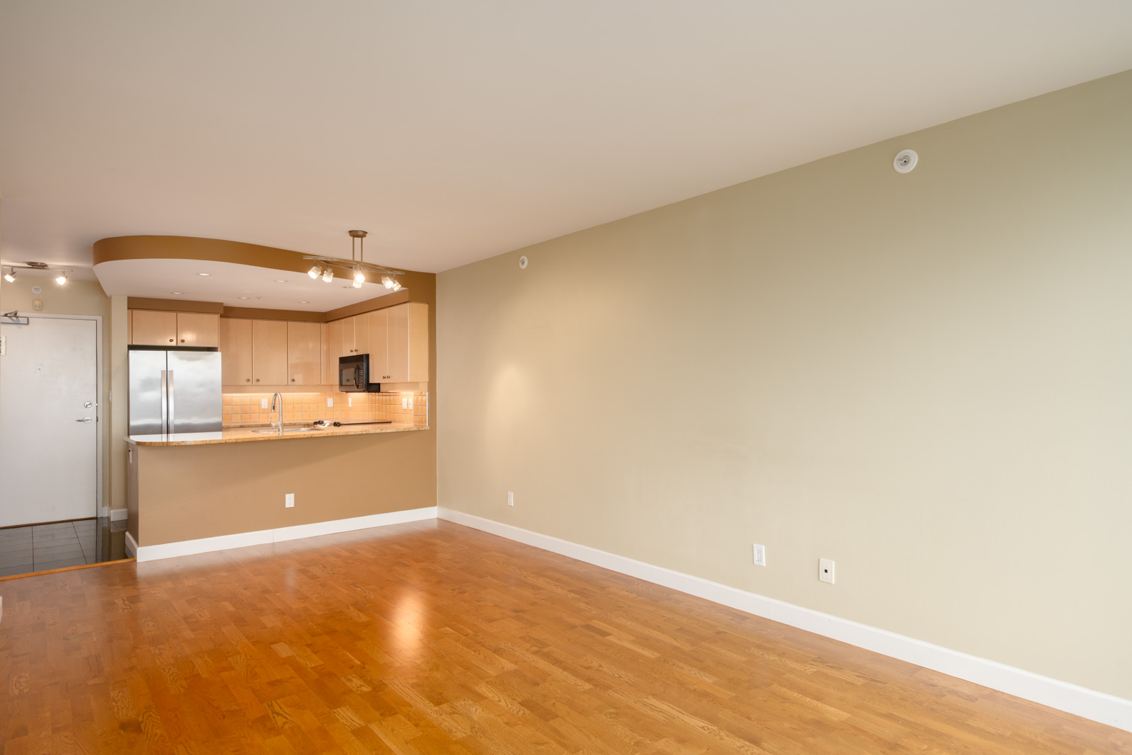 Unfurnished apartment at 1008 Cambie St, Vancouver, with hardwood floors, beige walls, and an open kitchen.