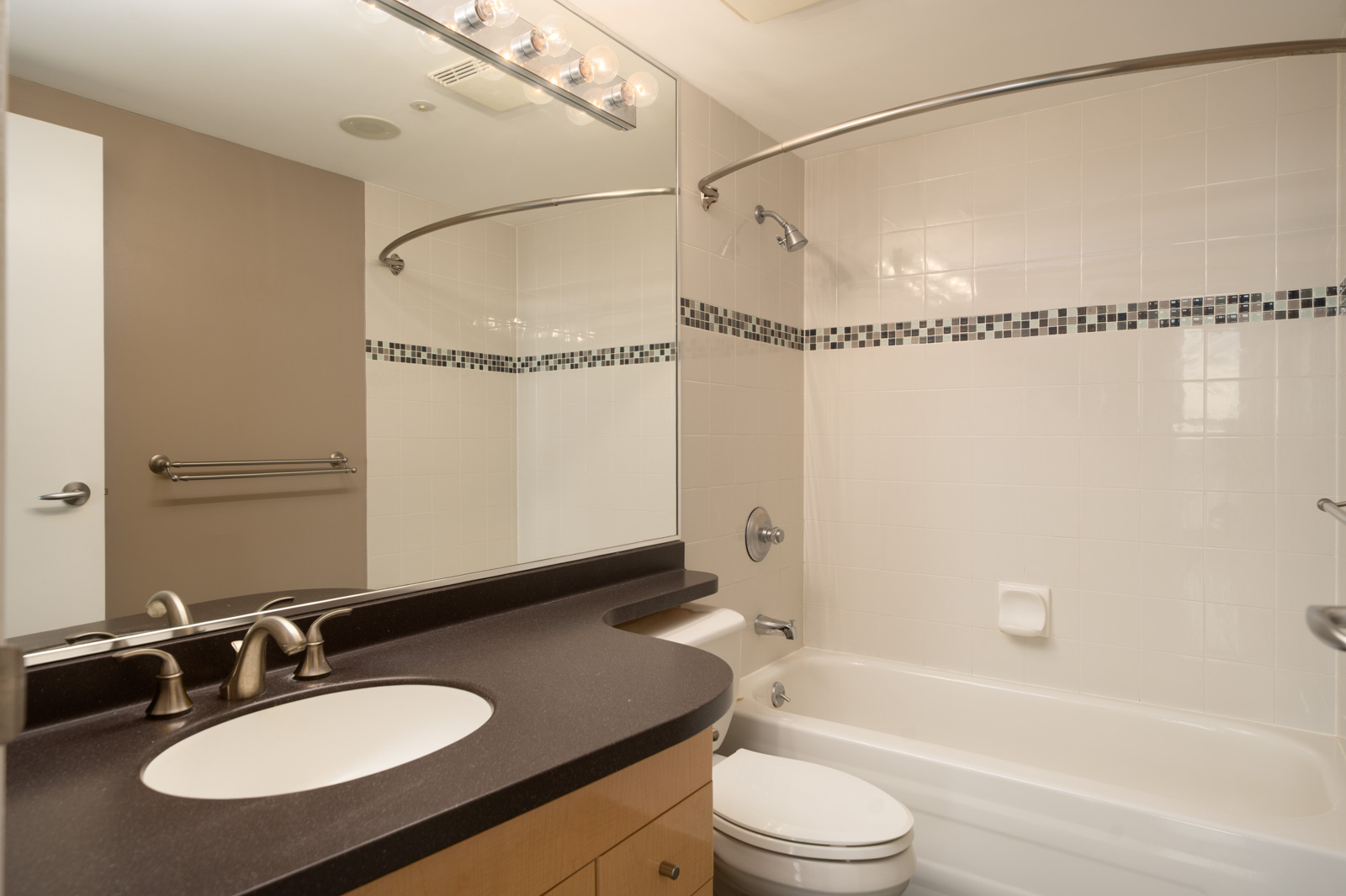 Modern Vancouver bathroom at 1008 Cambie St. featuring curved shower rod, mosaic tile above tub, wall mirror, and single-sink vanity.