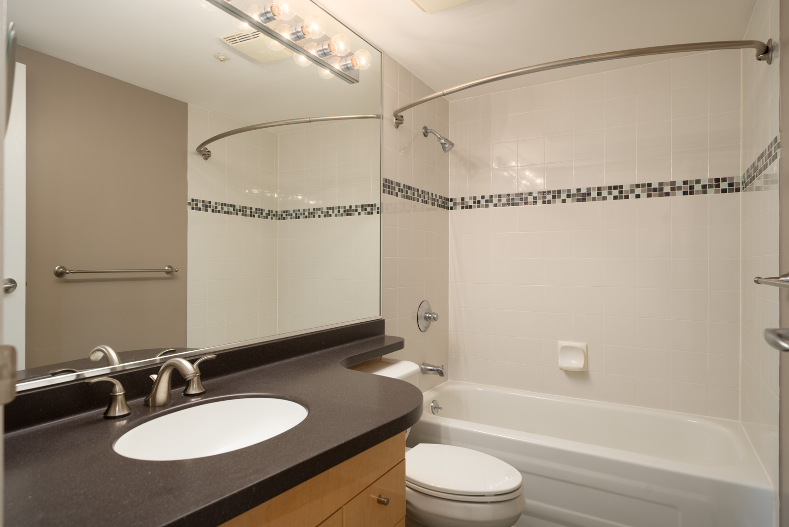 Modern bathroom at 1008 Cambie St, Vancouver with dark countertop, under-mount sink, large mirror, toilet, and tiled bathtub.
