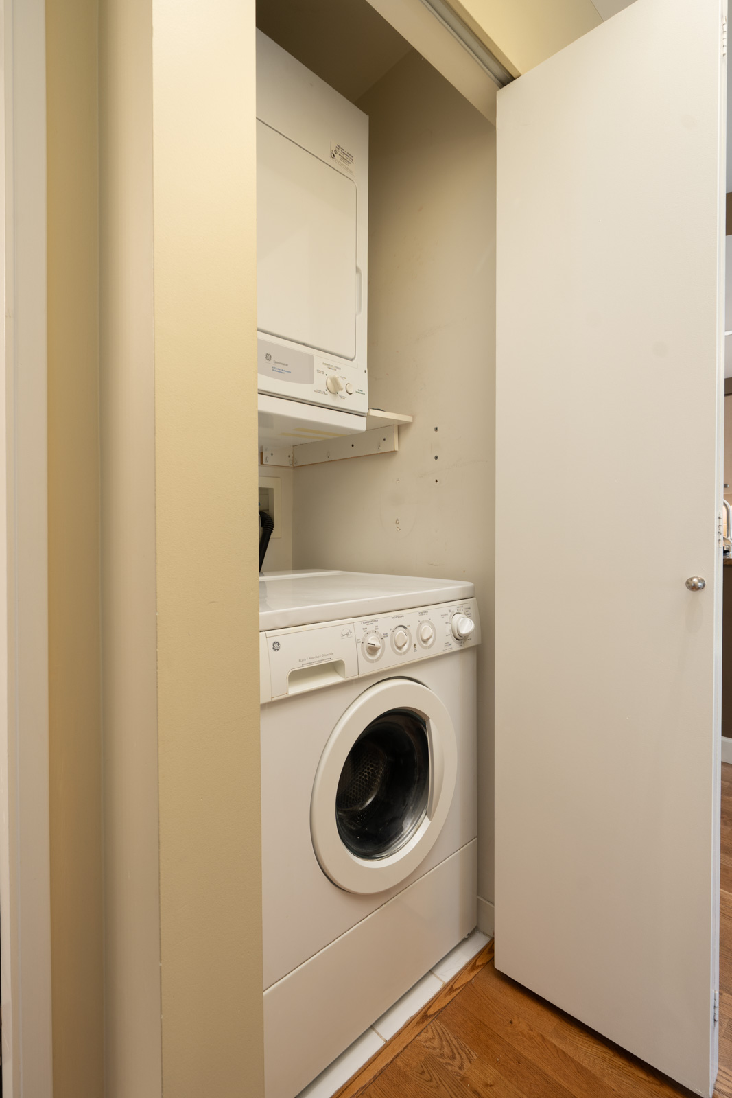 A stacked washer and dryer sit in a small closet with open white doors beside hardwood floors at 1008 Cambie St, Vancouver.