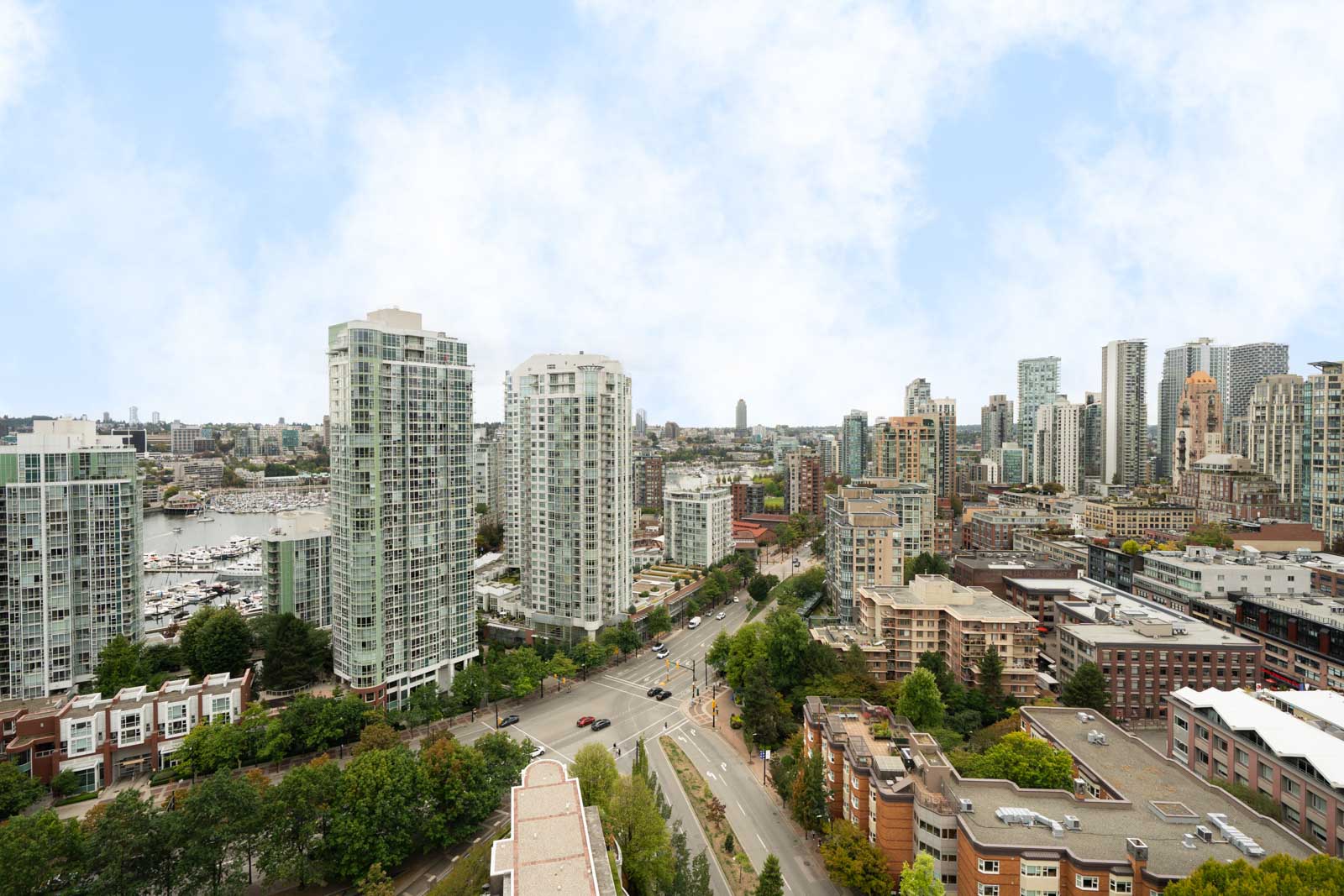 Vancouver cityscape with modern high-rises, tree-lined Cambie St, and a marina of boats beneath partly cloudy skies.