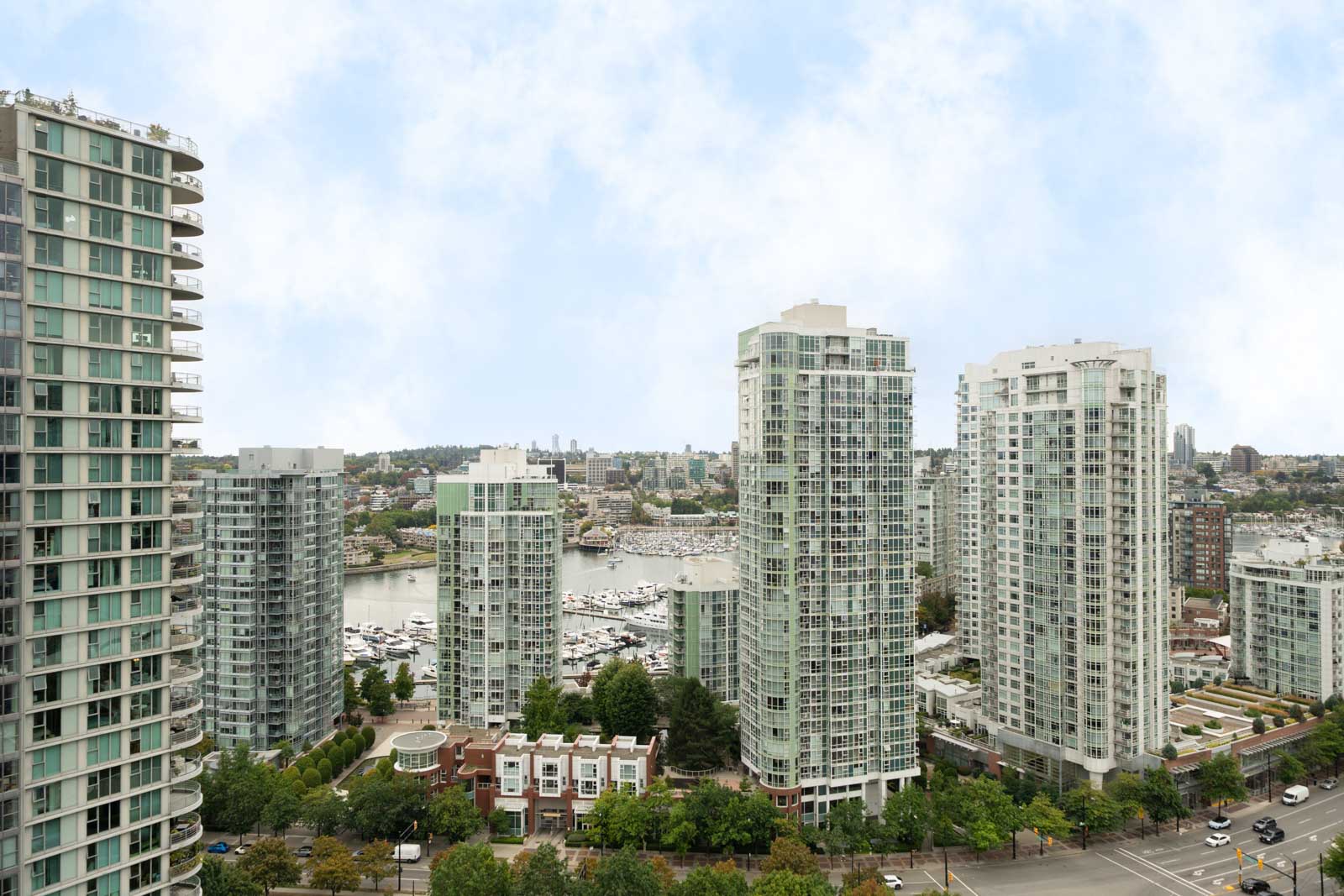 High-rise apartments overlook a marina with boats, trees, and roads, set against Vancouver’s skyline under cloudy skies from the 29th floor.