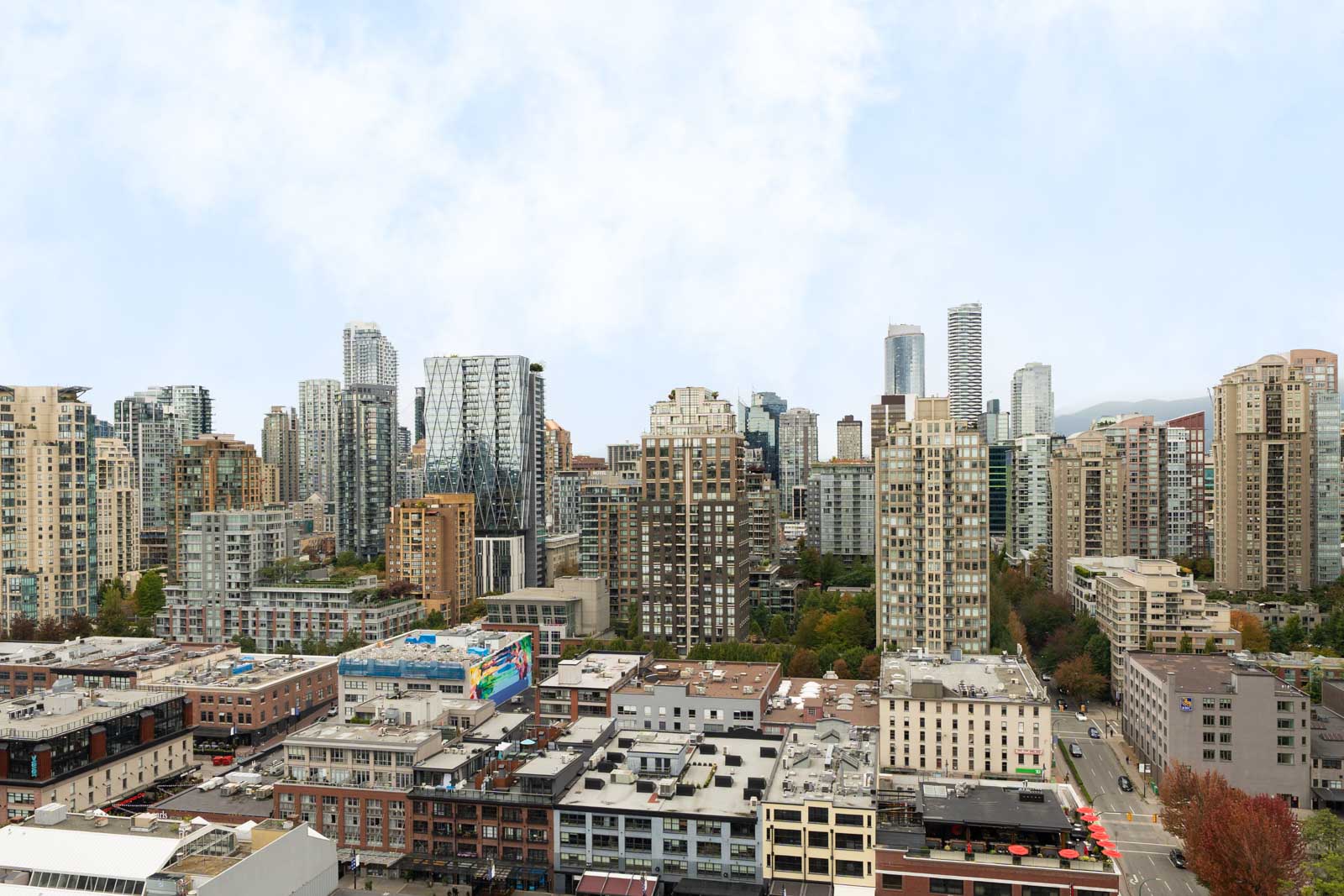 Vancouver city skyline with modern high-rise and mid-rise buildings, some trees, under a partly cloudy sky near 1008 Cambie St.