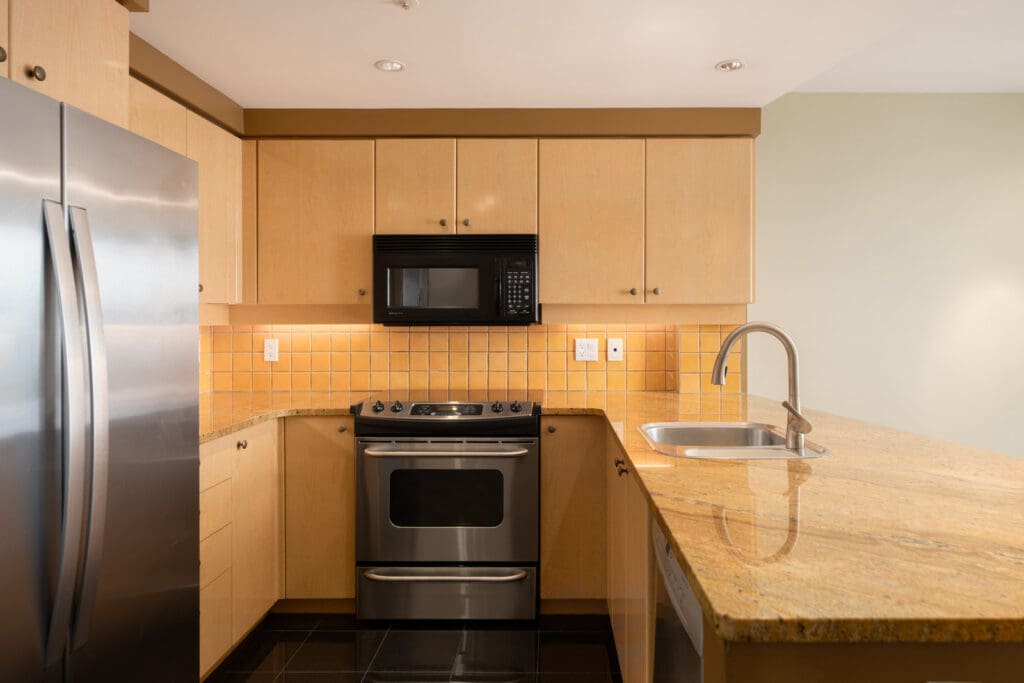Modern Vancouver kitchen with wood cabinets, stainless steel appliances, black microwave, yellow tile backsplash, and granite countertop on Cambie St.