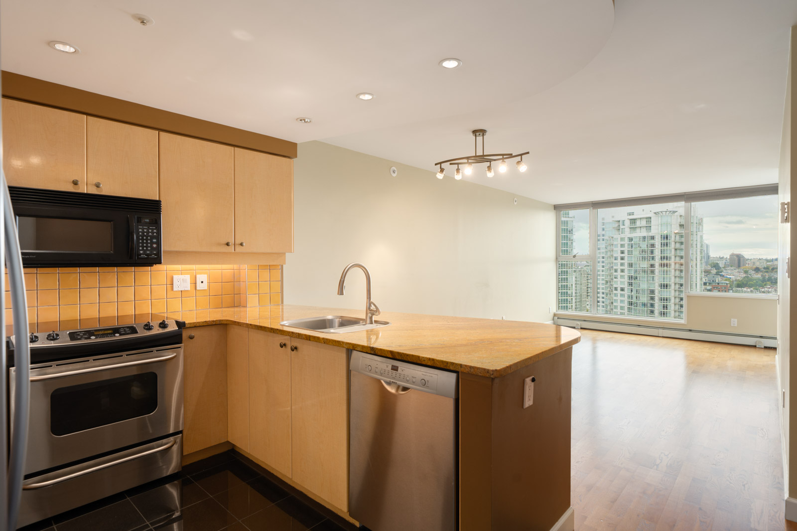 Modern kitchen with stainless appliances, light wood cabinets, island sink, and open living area with city views at 1008 Cambie St, Vancouver.