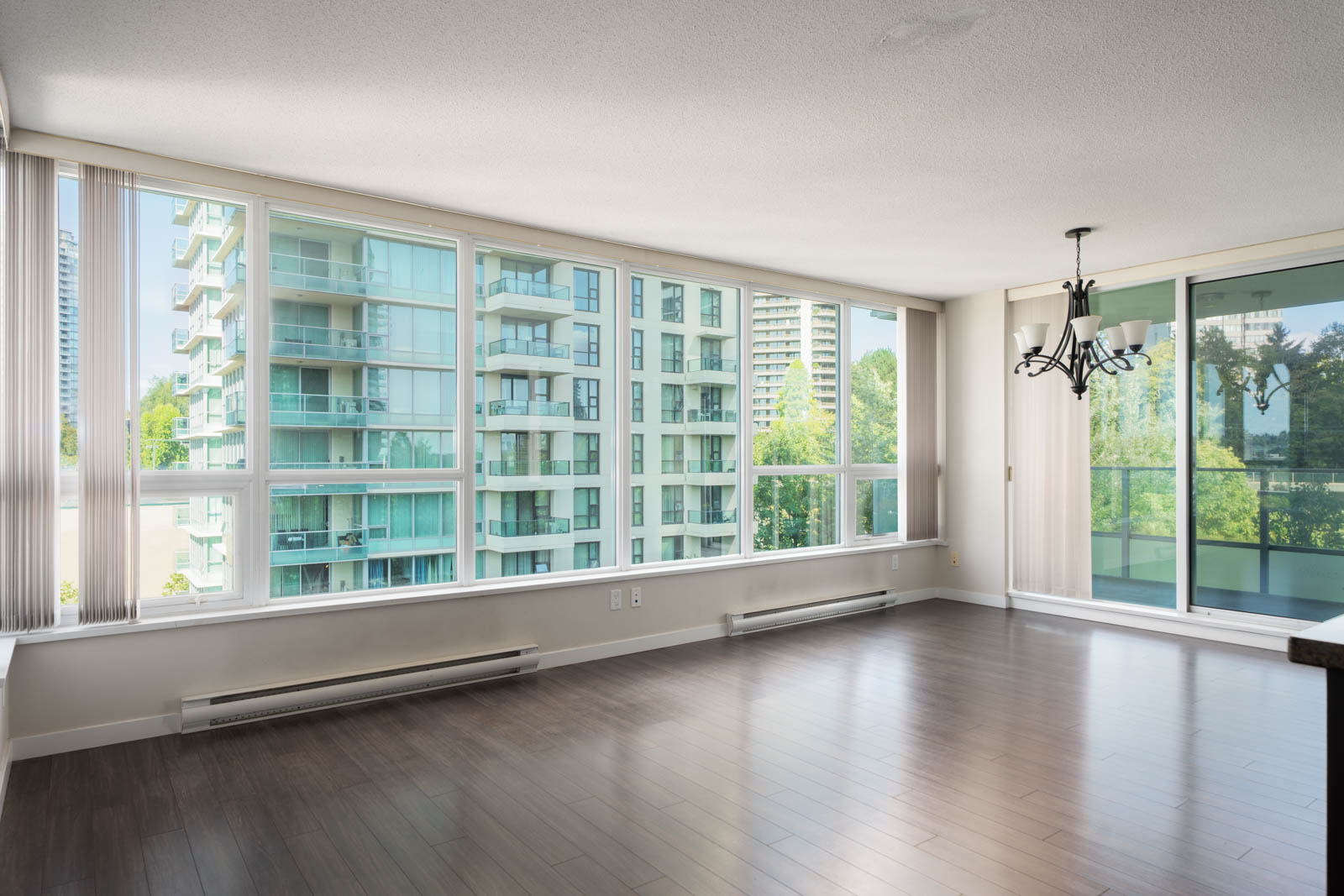 Modern empty living room with hardwood floors, large windows, and chandelier on 7th floor, Douglas Rd, Vancouver.