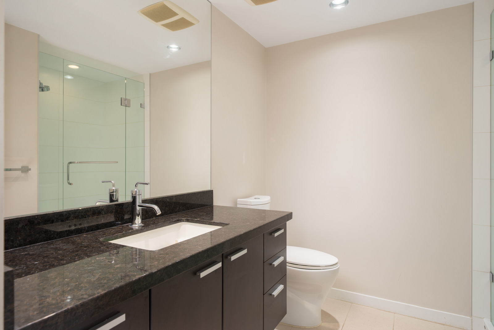 Modern bathroom at 2232 Douglas Rd, Vancouver with dark wood vanity, black countertop, wall mirror, toilet, and glass shower.