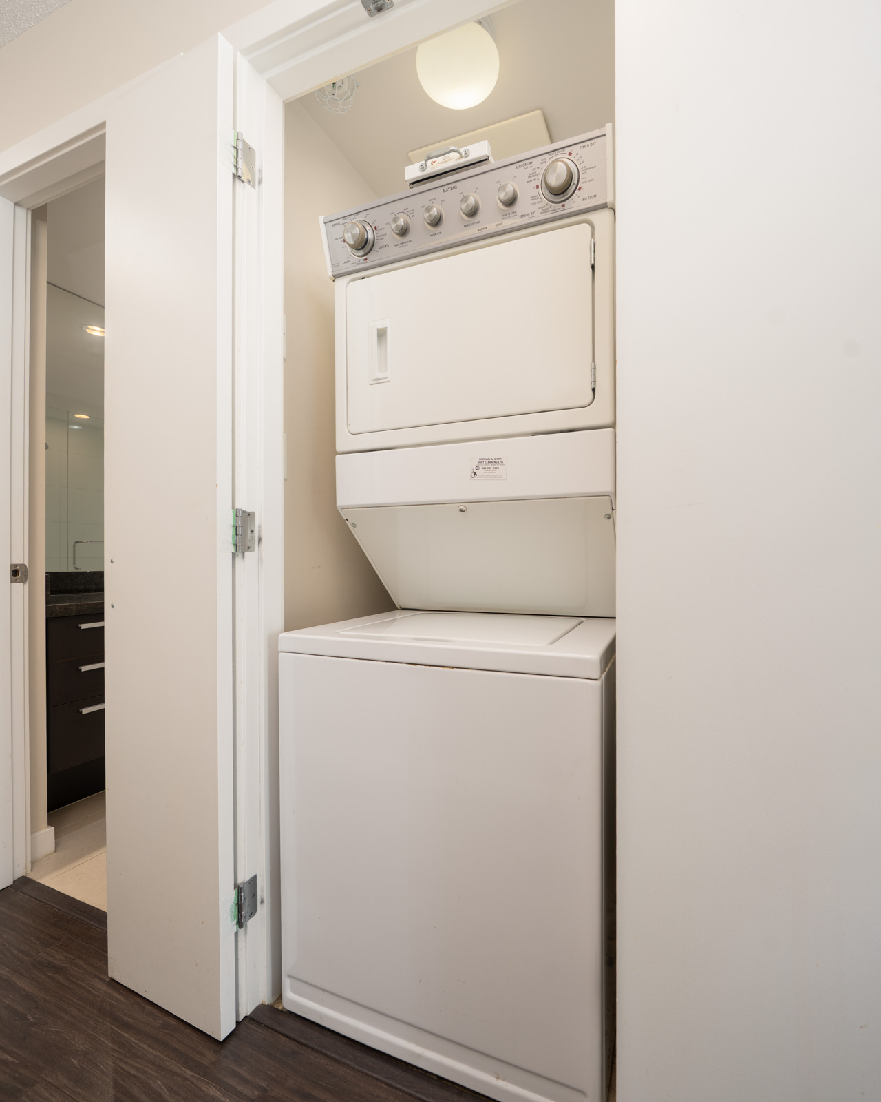 Stacked washer and dryer in a compact laundry closet with white walls and wood floors in a 7th Floor Vancouver building.