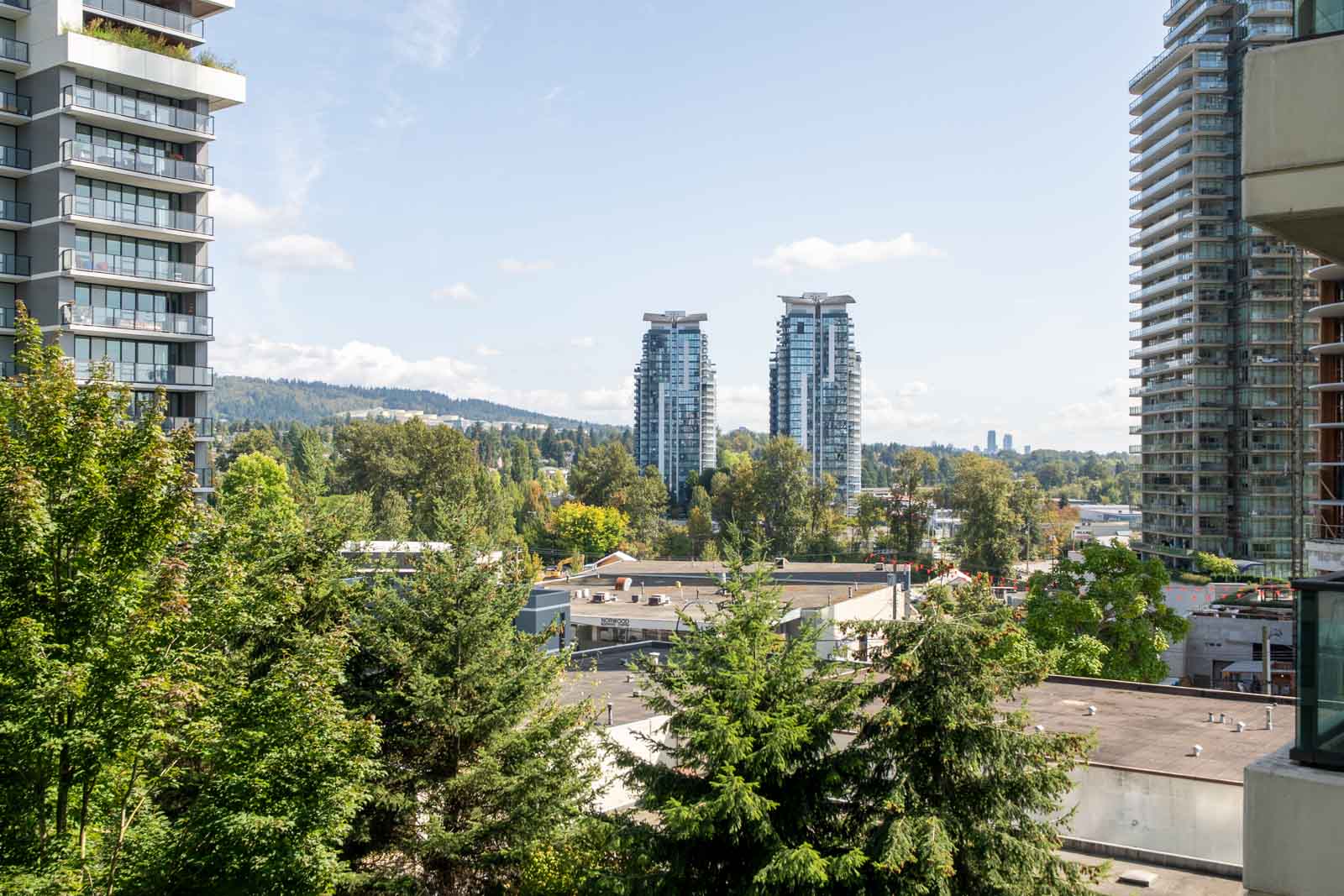 Seventh-floor view of tall apartments, treetops, and low-rise roofs under a clear sky in Vancouver’s Douglas Rd area.