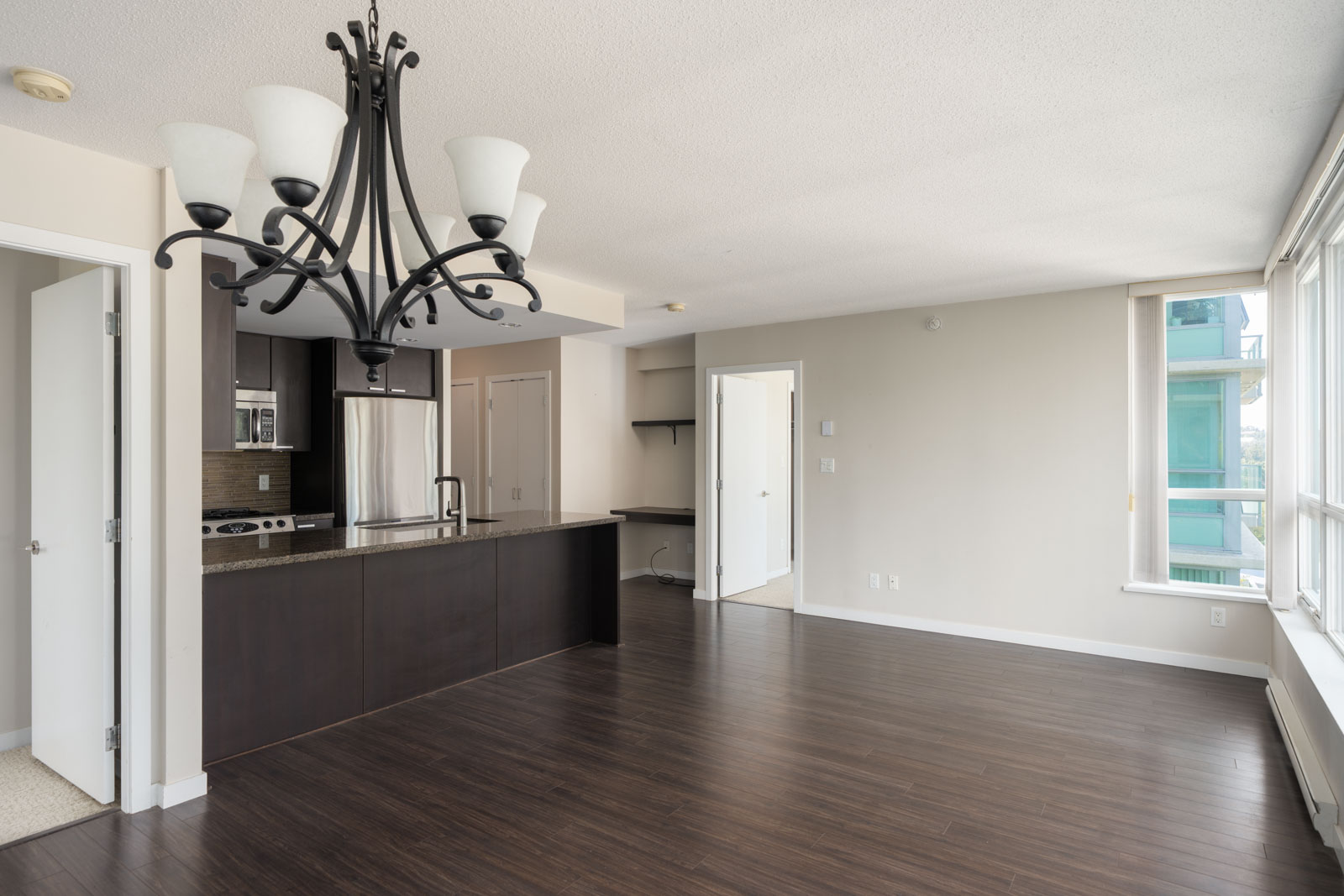 Unfurnished modern apartment at 2232 Douglas Rd, Vancouver. Dark wood floors, open kitchen, large windows, black chandelier.