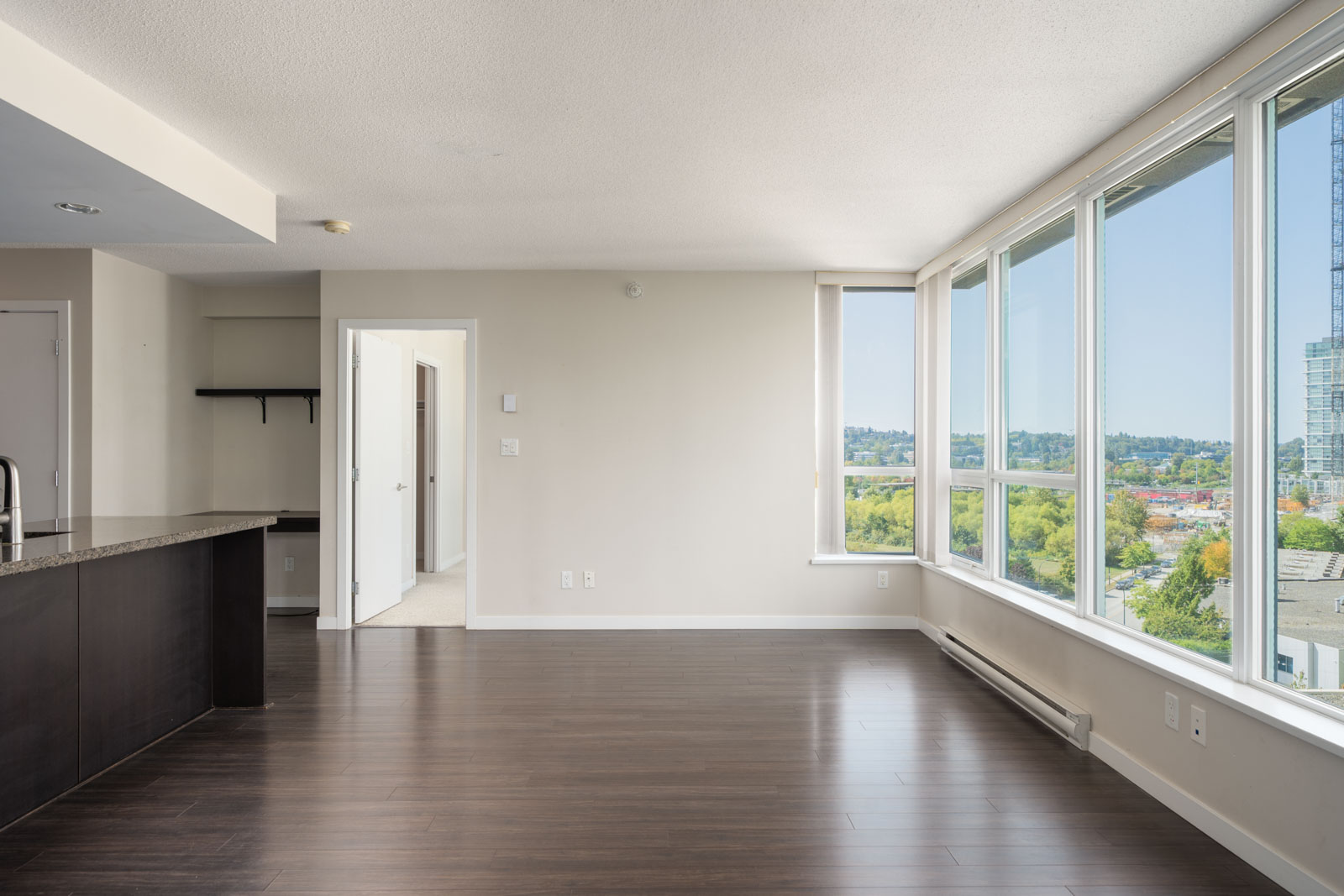 Unfurnished Vancouver apartment with dark wood floors, large windows, white walls, open kitchen, and city view on Douglas Rd.