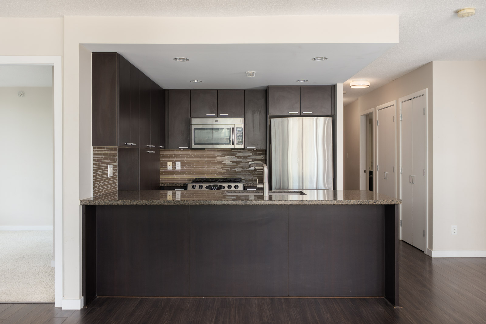 Modern kitchen with dark cabinets, stainless steel appliances, granite counters, and tile backsplash in a 7th floor Vancouver home.