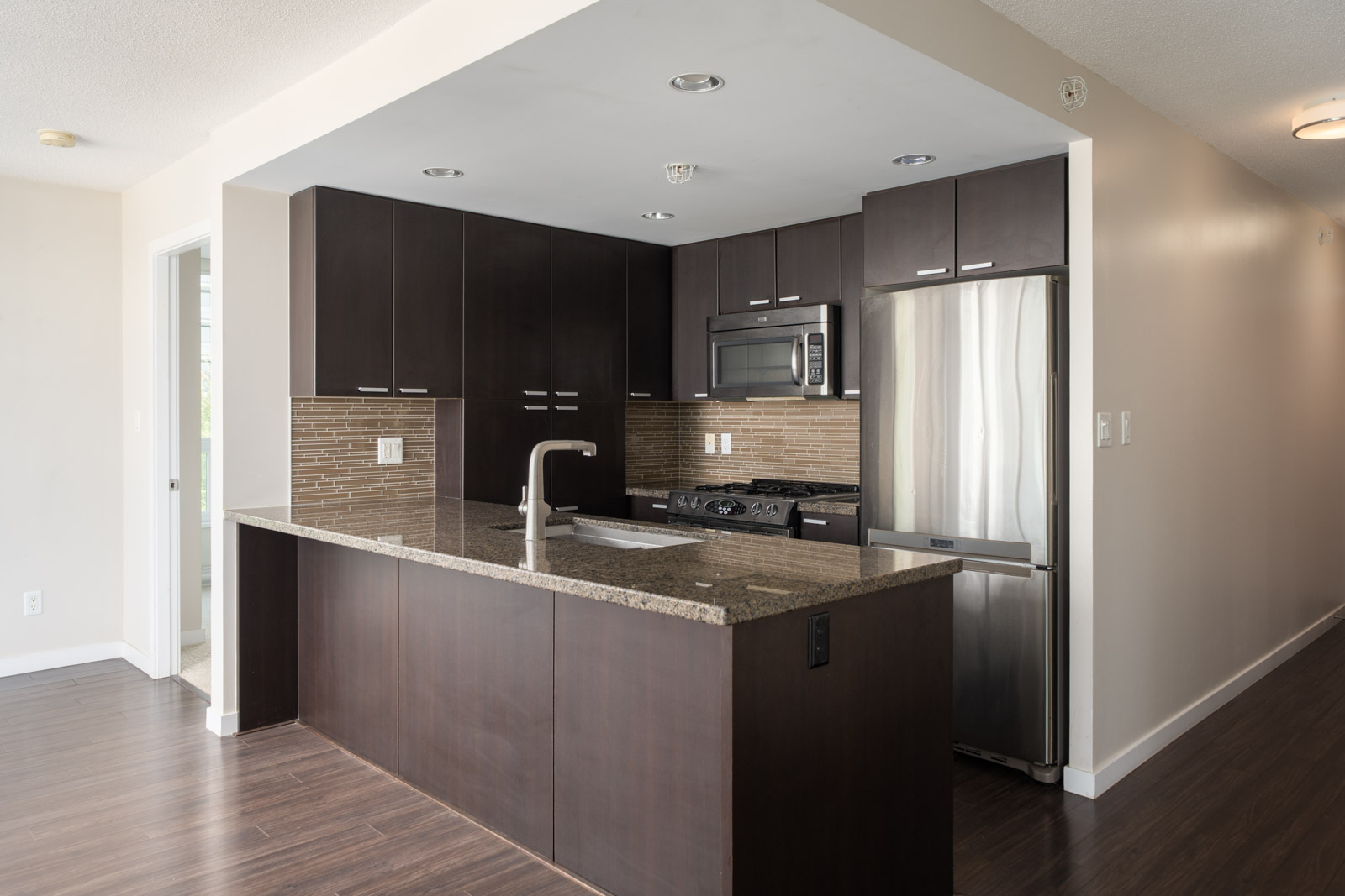 Modern kitchen at 2232 Douglas Rd, 7th Floor Vancouver with dark wood cabinets, stainless appliances, granite island sink.