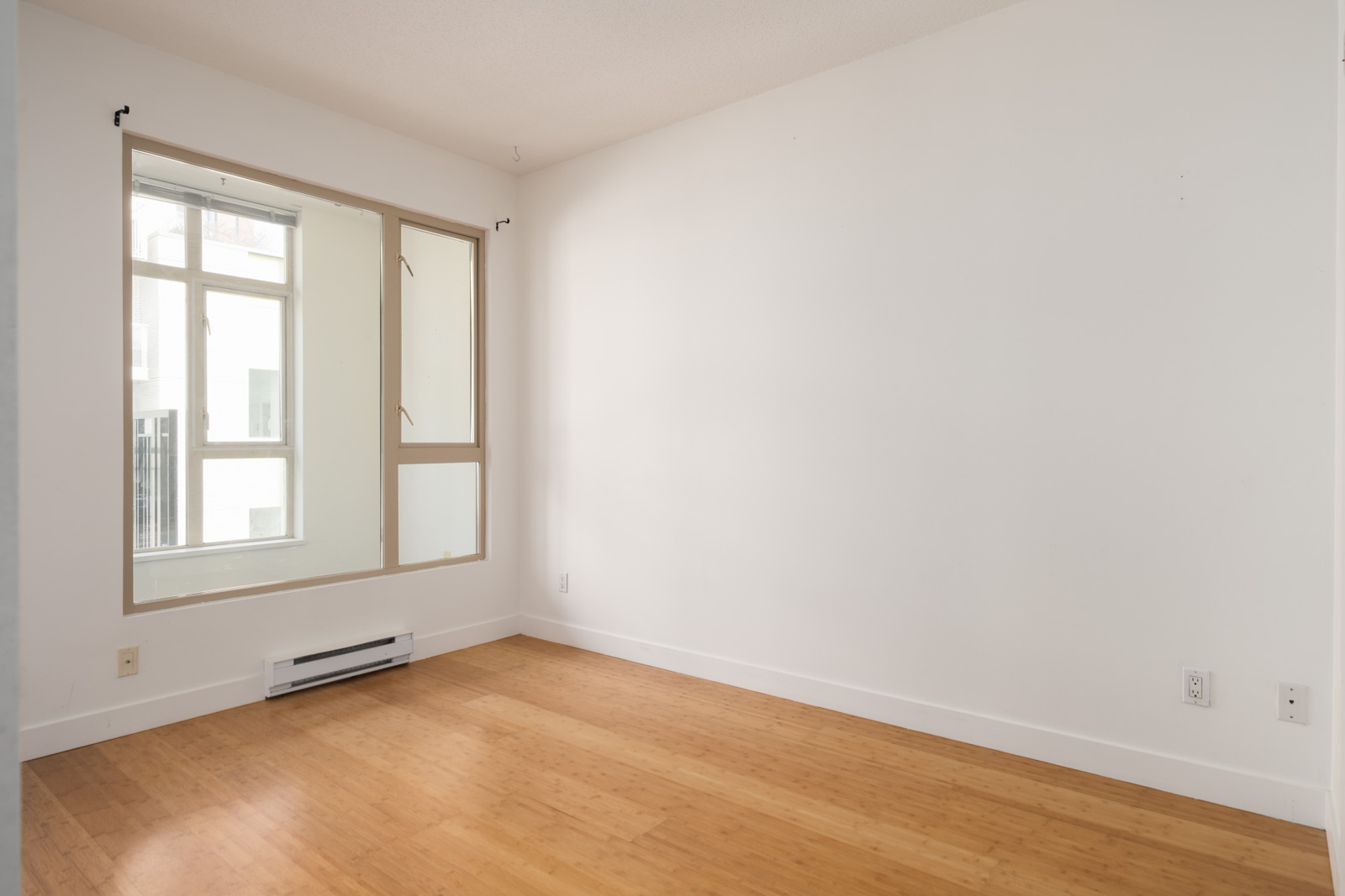 Vacant room on the 4th floor at 205 E 10th Ave, Vancouver with white walls, large window, light wood floor, and heater.