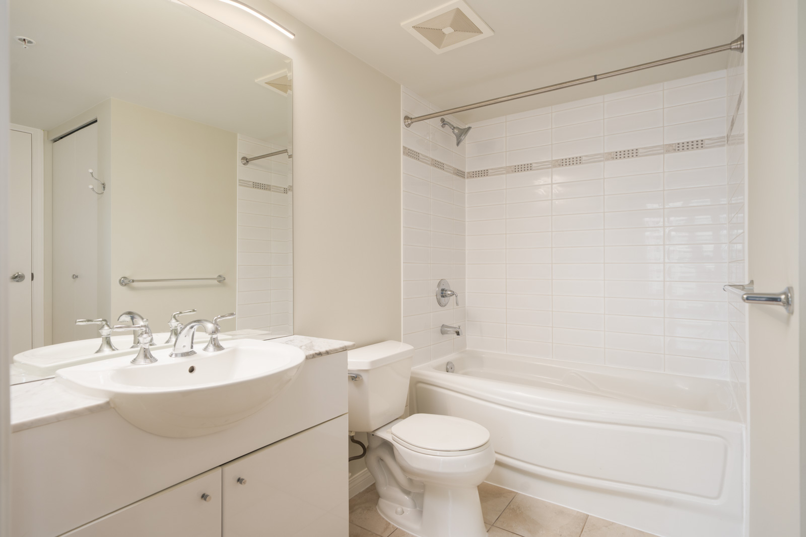 Modern bathroom with white sink, toilet, and bathtub; large mirror; tiled walls and floor; 12th Floor, 188 E Esplanade, North Vancouver.