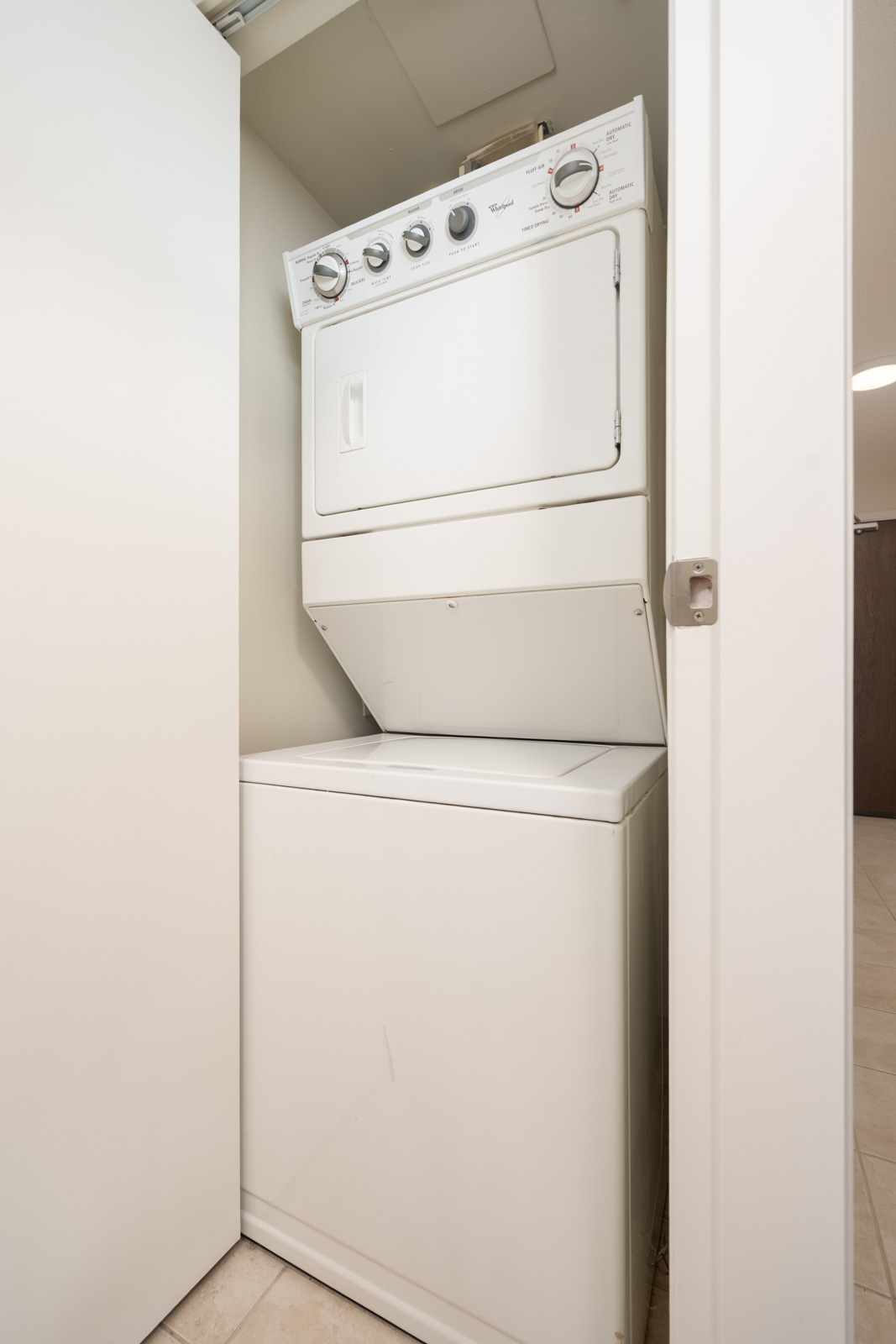 Stacked washer and dryer in a small open closet with white doors and beige tile floor at 188 E Esplanade, 12th floor, North Vancouver.