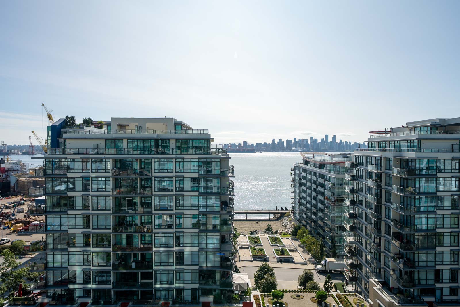 Two glass apartment buildings frame a harbor view with the Vancouver skyline in the distance under a clear sky.