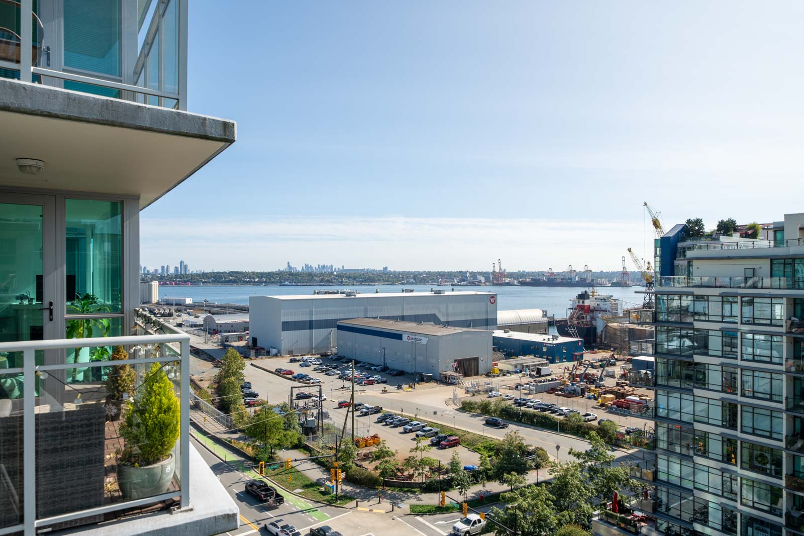 Balcony view at 188 E Esplanade, North Vancouver: warehouses, cranes, parked cars, and distant city skyline under clear sky.