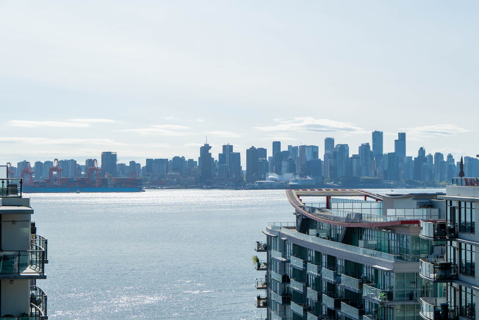 City skyline across the water with modern buildings—like 188 E Esplanade, North Vancouver—and sunlight on the surface.