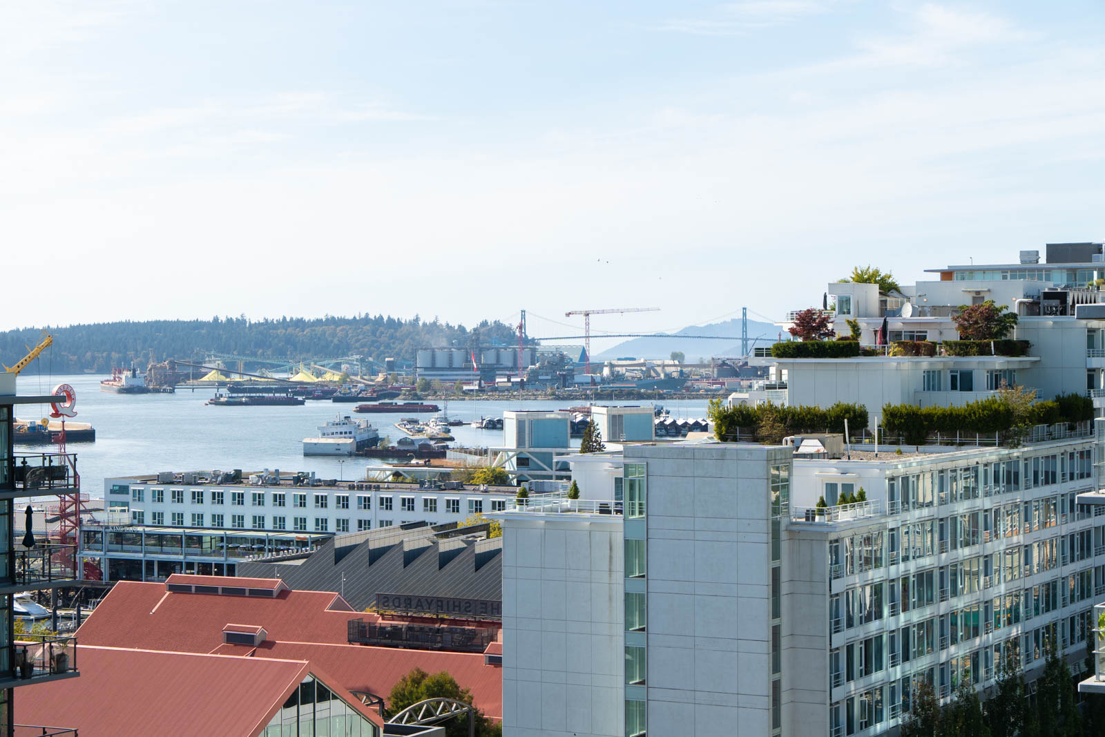 Modern buildings at 188 E Esplanade, North Vancouver, with ships and cranes by the water and distant hills under clear skies.