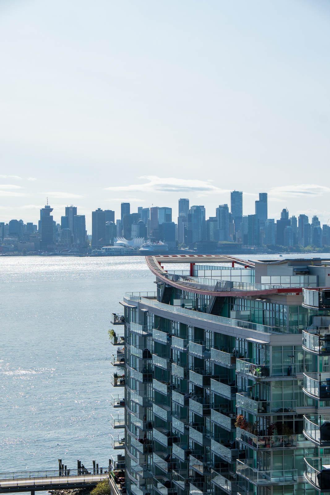 A glass-fronted apartment at 188 E Esplanade, North Vancouver, overlooks water with a city skyline and skyscrapers behind.