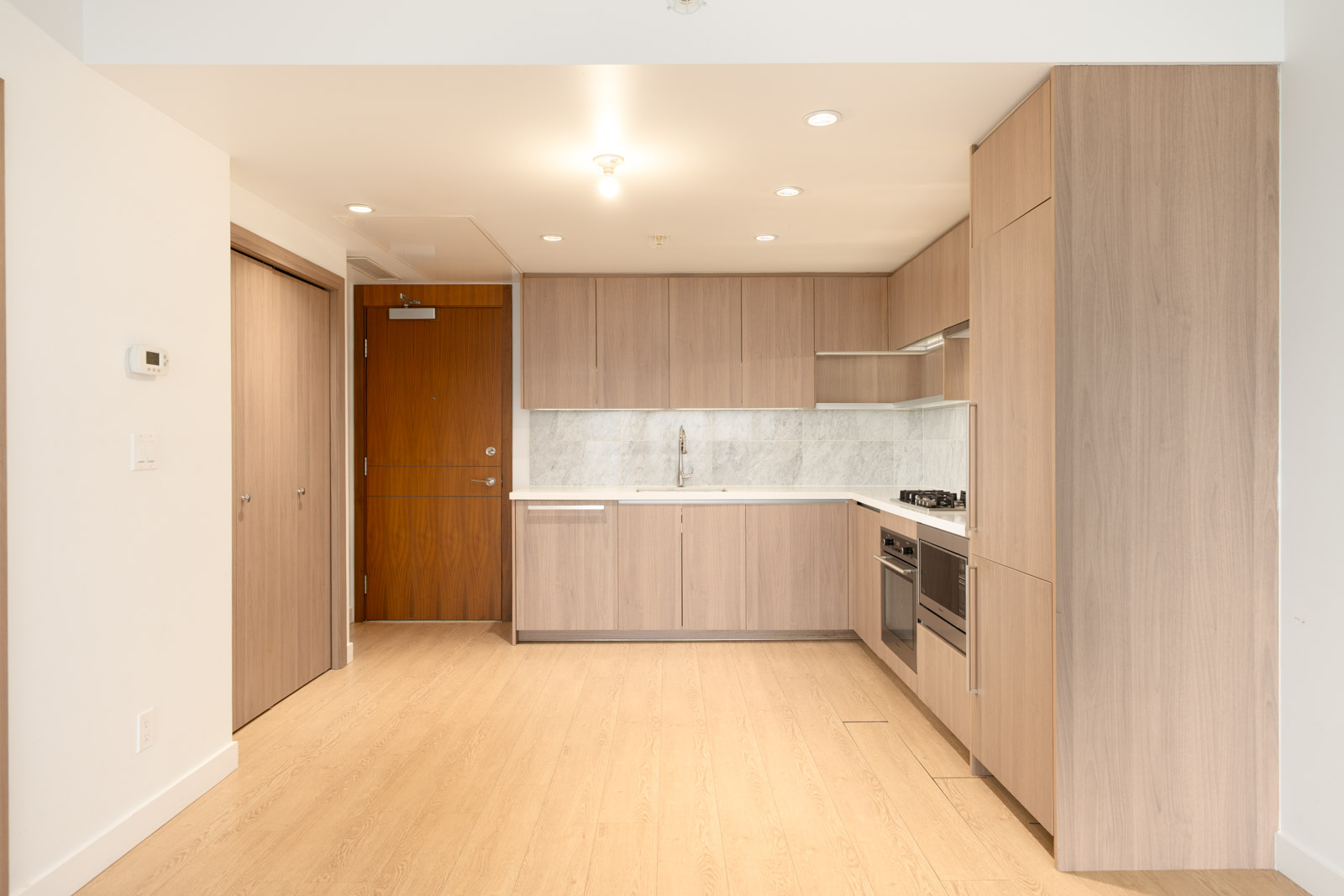 Modern kitchen with light wood cabinets, built-ins, marble backsplash, light floors, and white walls in a 27th floor Burnaby condo.