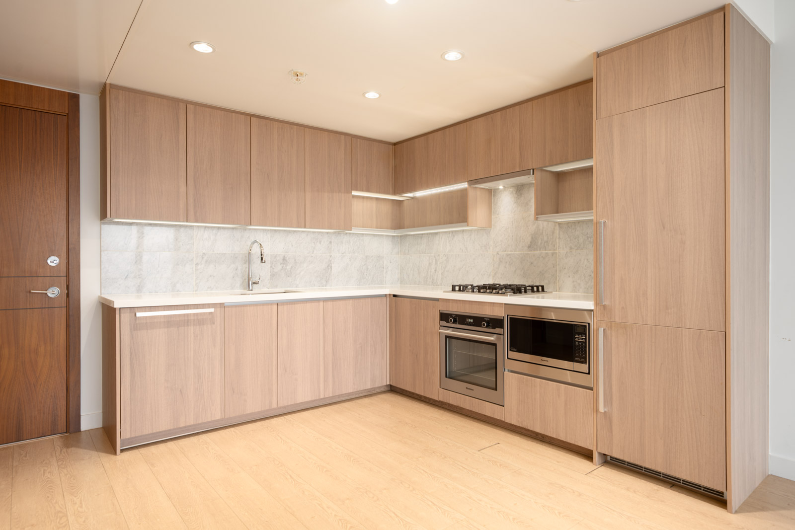 Modern kitchen with light wood cabinets, built-in oven, microwave, gas stove, marble backsplash; 27th floor on Nelson Ave, Burnaby.