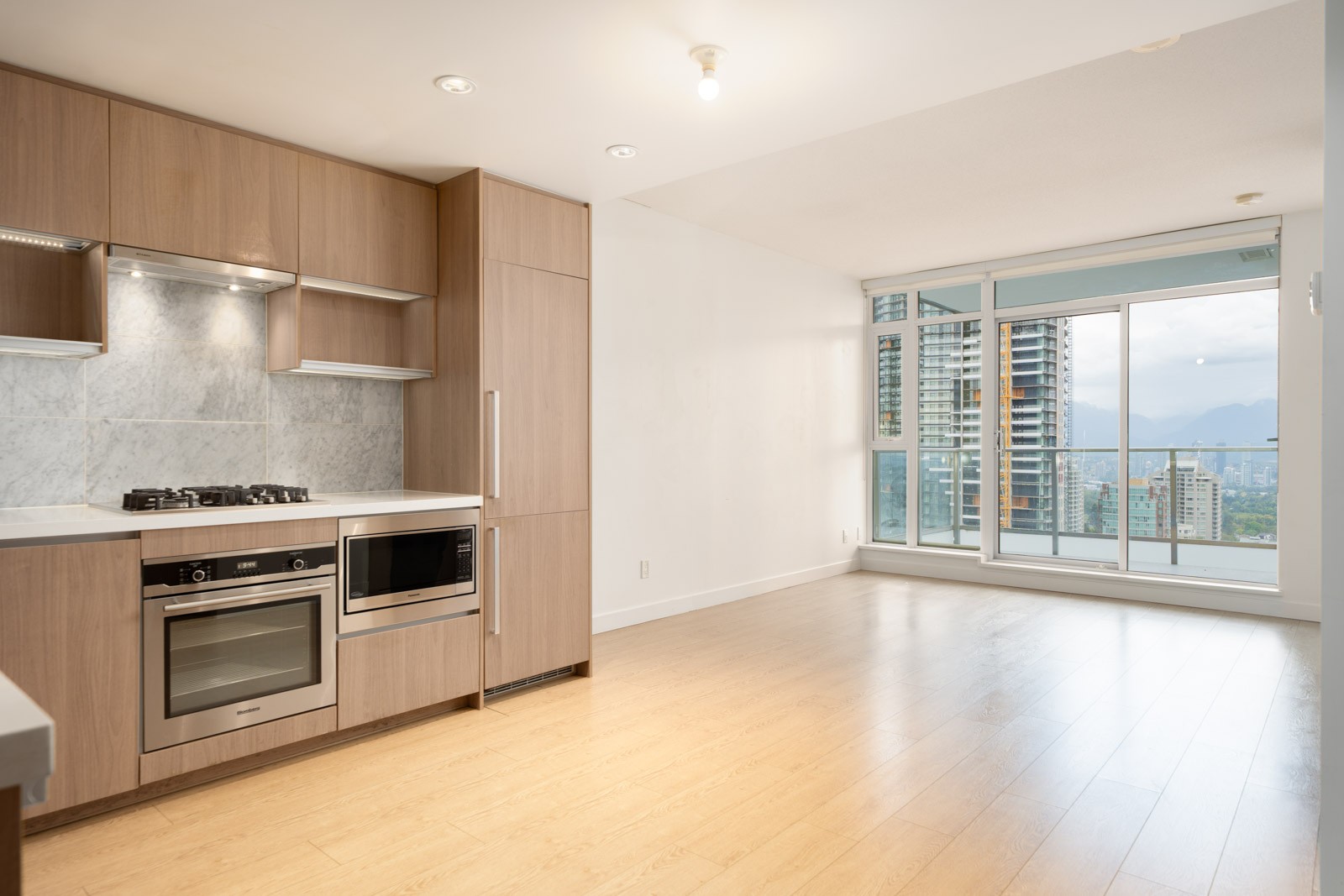 Unfurnished apartment at 6538 Nelson Ave, Burnaby with wood floors, built-in appliances, large windows, and balcony city views.