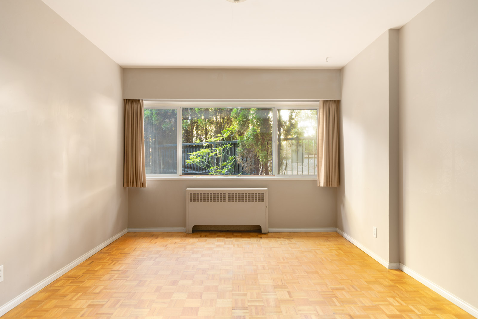 Empty room with light walls, parquet floors, large window with beige curtains, and radiator below on W 41st Ave in Vancouver.