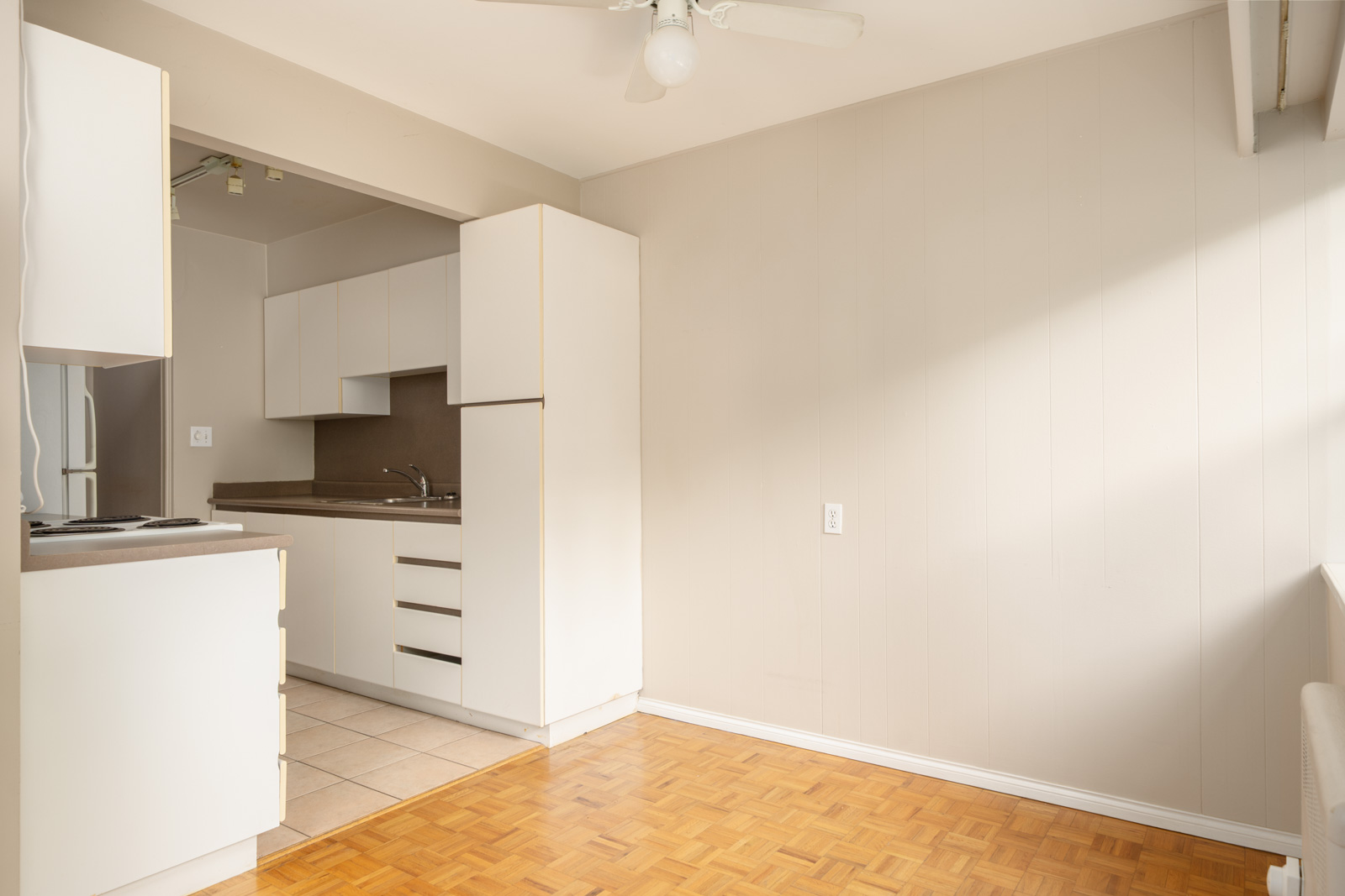 Bright, empty kitchen with white cabinets, beige counters, mix of tile and parquet floors, ceiling fan, and neutral walls in Vancouver.