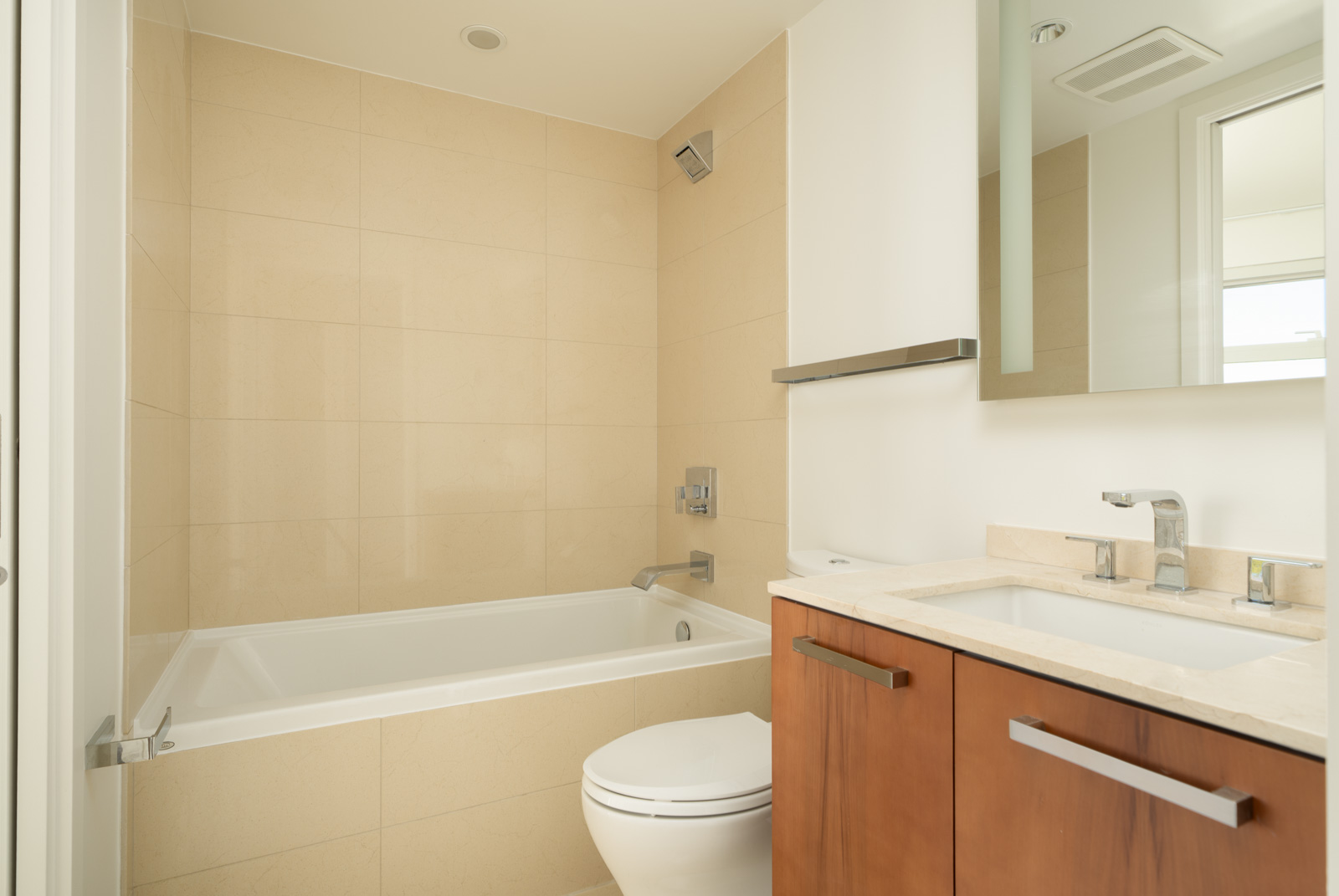 Modern bathroom at 1565 West 6th Ave, Vancouver, with a tub-shower combo, beige tiles, toilet, and vanity with brown cabinetry.